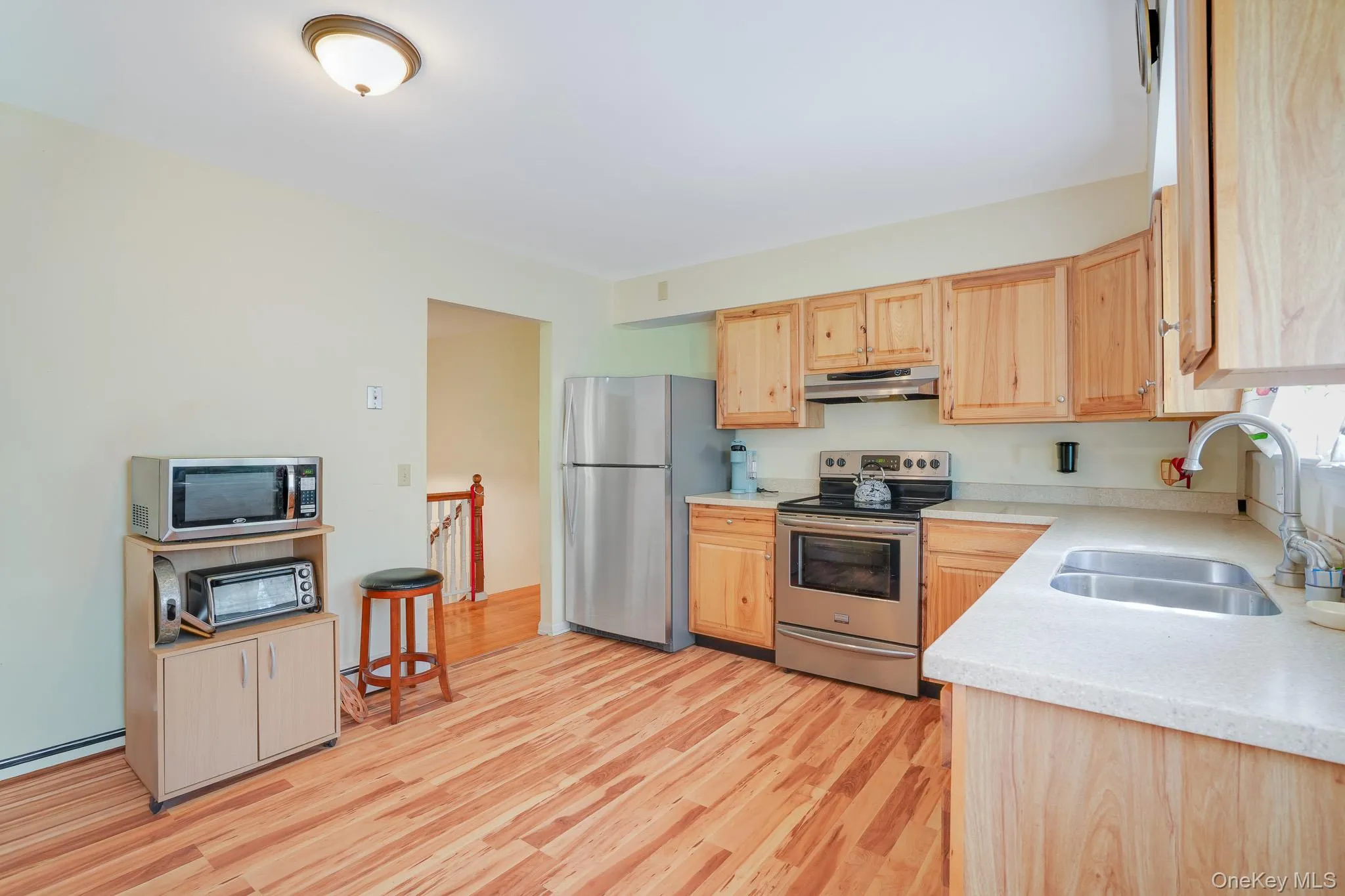 Kitchen featuring wood-finish flooring, light-toned cabinetry, stainless steel appliances, a double basin sink, and ample counter space Kitchen featuring wood-finish flooring, light-toned cabinetry, stainless steel appliances, a double basin sink, and ample counter space