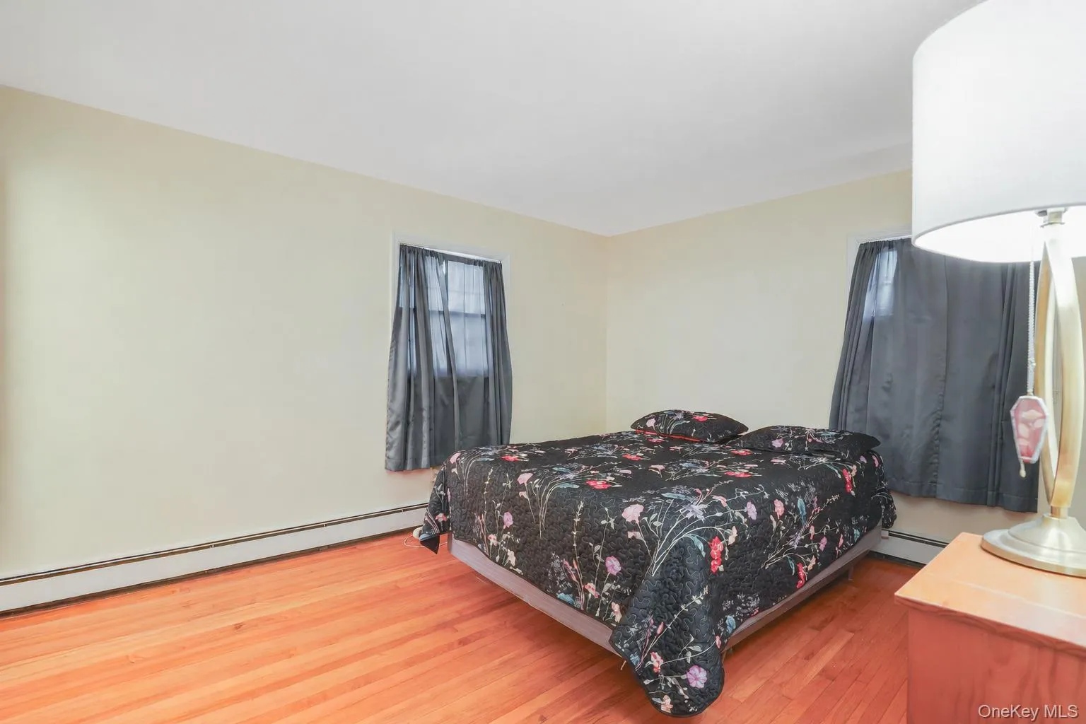 Bright bedroom featuring wood-finish flooring, two windows, and neutral wall tones Bright bedroom featuring wood-finish flooring, two windows, and neutral wall tones