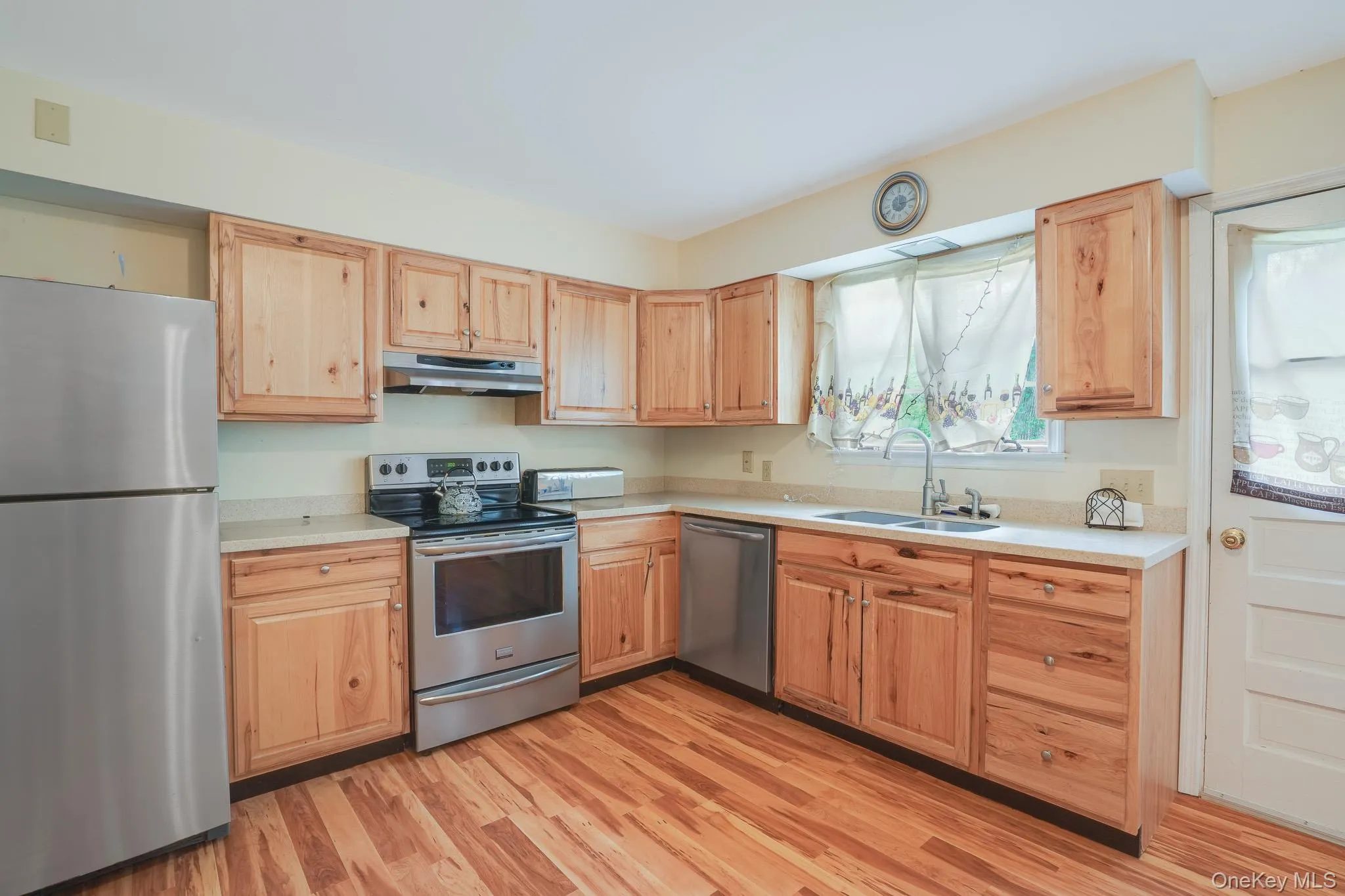Kitchen featuring wood-finish flooring, light wood cabinetry, stainless steel appliances, and a double basin sink Kitchen featuring wood-finish flooring, light wood cabinetry, stainless steel appliances, and a double basin sink