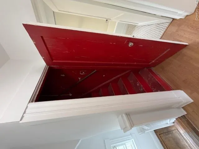 Rich red painted door opening to a staircase, complemented by light wood-finish flooring Rich red painted door opening to a staircase, complemented by light wood-finish flooring