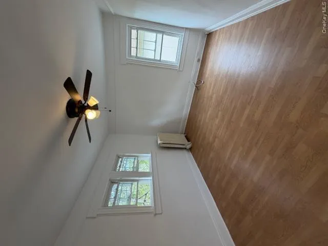 Room featuring wood-finish flooring, a ceiling fan with integrated lighting, and multiple windows with white trim Room featuring wood-finish flooring, a ceiling fan with integrated lighting, and multiple windows with white trim