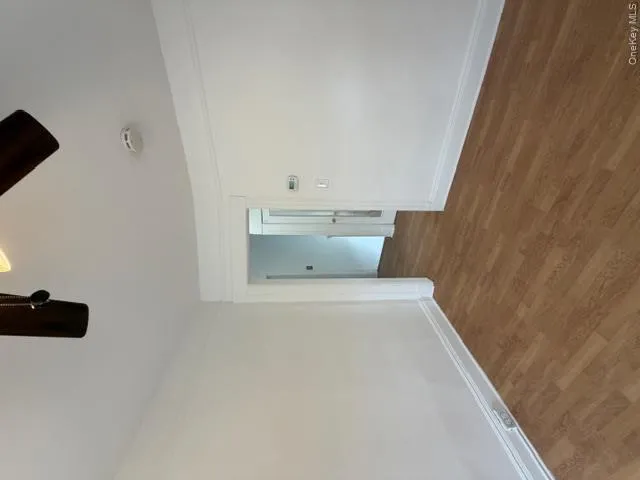 Room featuring wood-finish flooring, white walls, and a ceiling fan with integrated lighting Room featuring wood-finish flooring, white walls, and a ceiling fan with integrated lighting