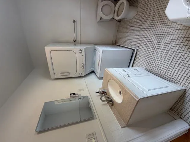 White bathroom vanity with a light-toned countertop, a rectangular mirror, and an adjacent stackable washer and dryer unit White bathroom vanity with a light-toned countertop, a rectangular mirror, and an adjacent stackable washer and dryer unit