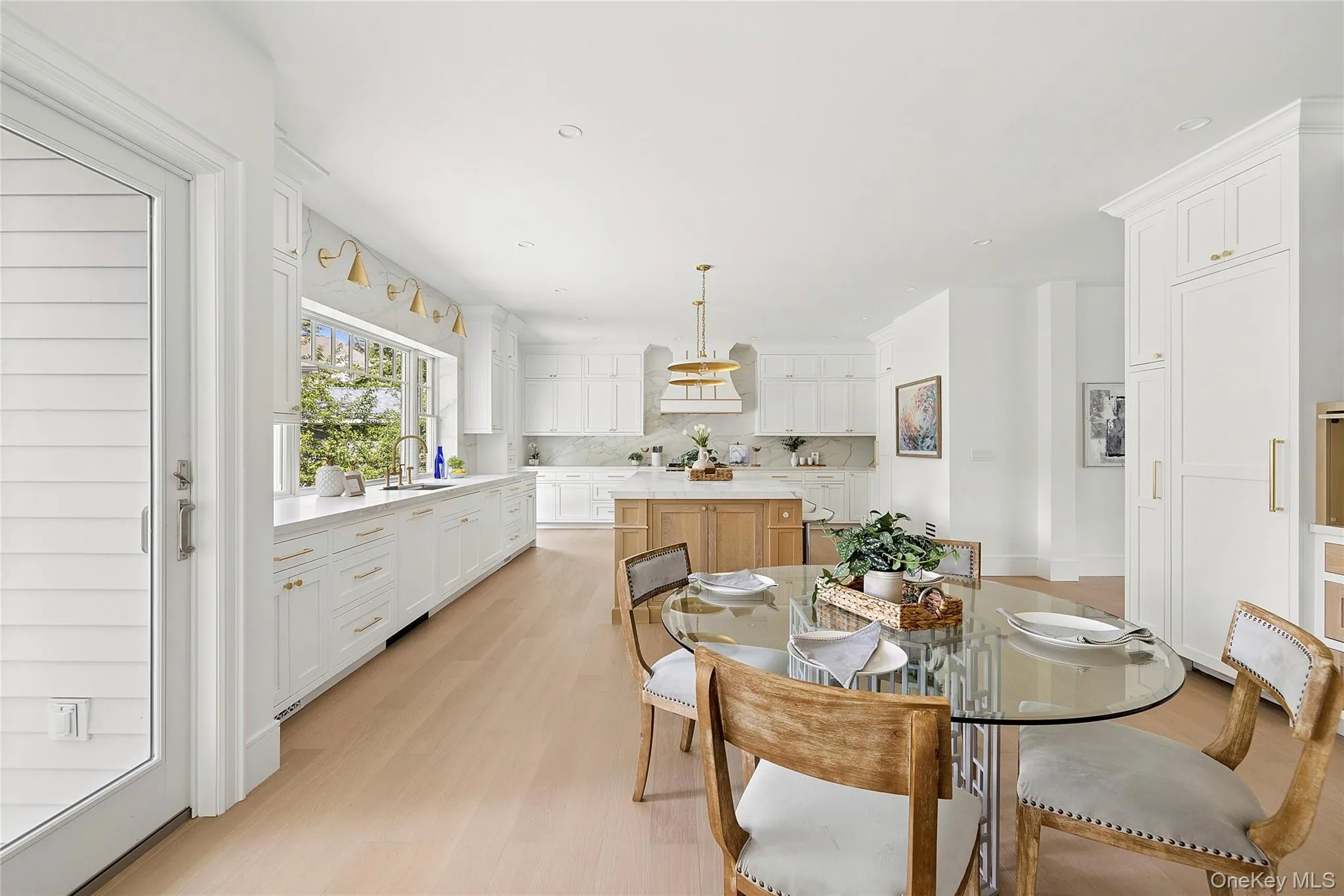 Open-concept kitchen featuring extensive white cabinetry, light wood-finish flooring, a central island with a wood base, and a wall of windows Open-concept kitchen featuring extensive white cabinetry, light wood-finish flooring, a central island with a wood base, and a wall of windows