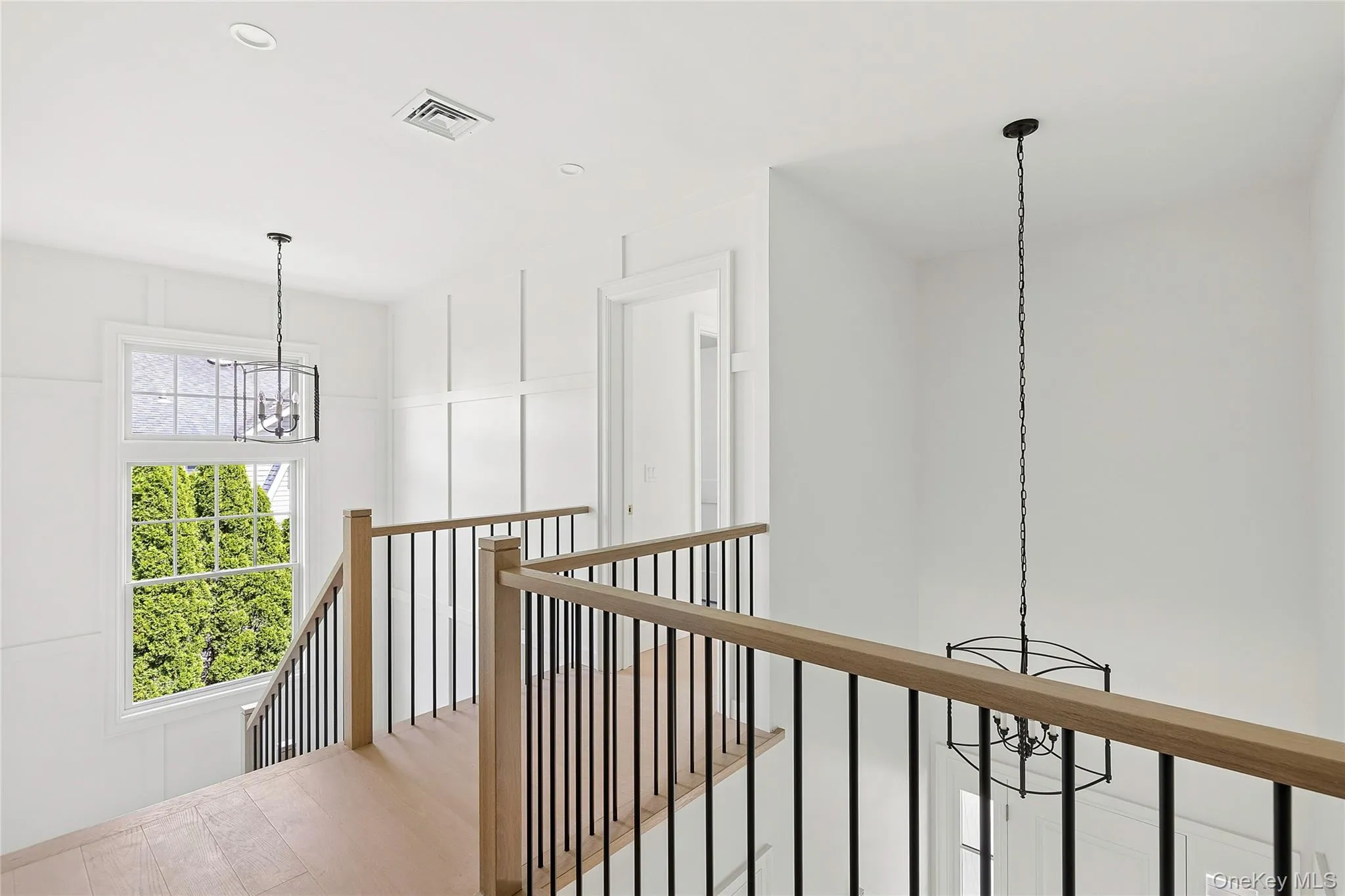 Staircase featuring wood-finish flooring, light wood handrails with black metal balusters, and white wall paneling Staircase featuring wood-finish flooring, light wood handrails with black metal balusters, and white wall paneling