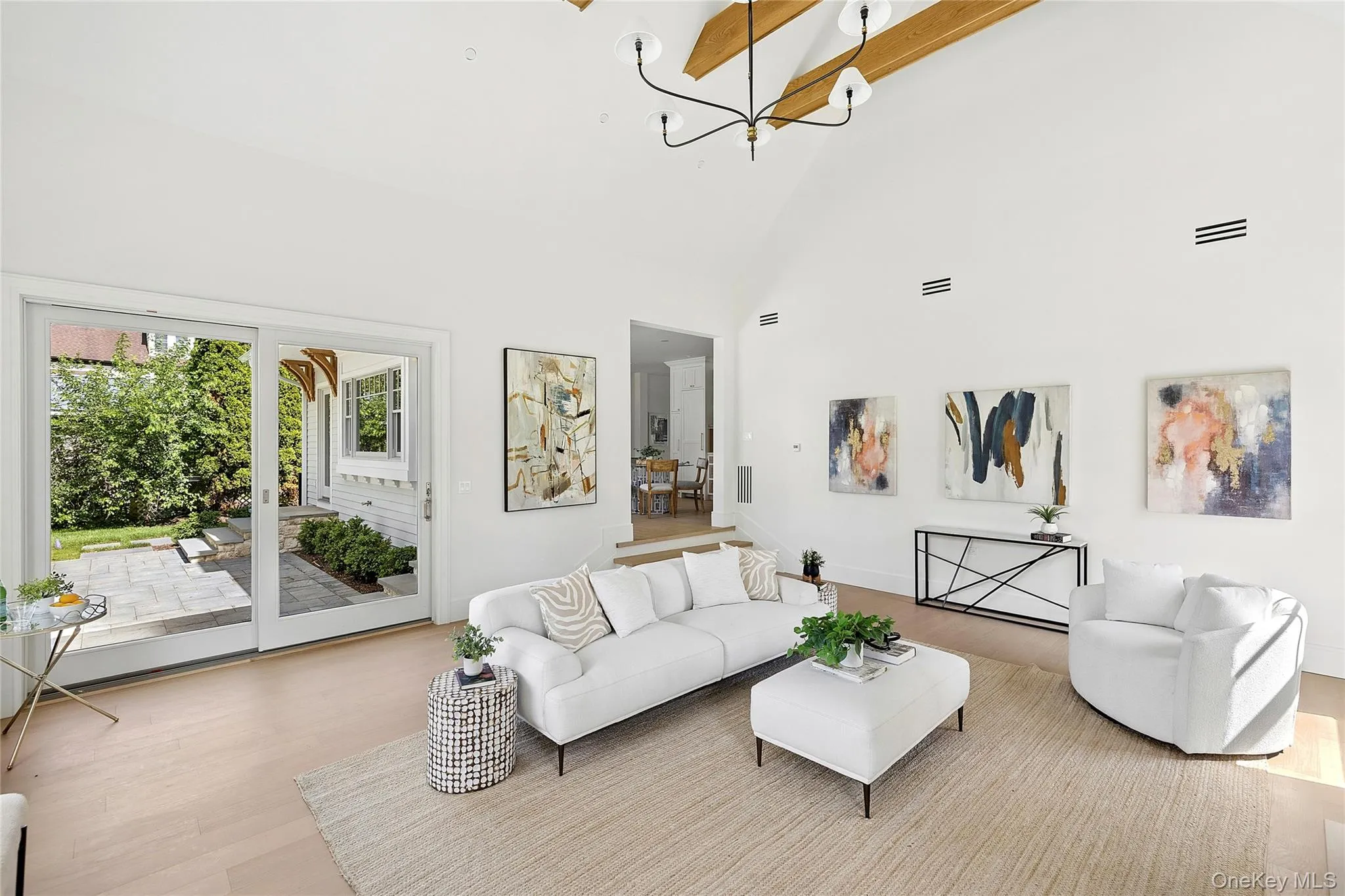 Spacious living area featuring a vaulted ceiling with exposed wood beams, a contemporary chandelier, and light wood-finish flooring Spacious living area featuring a vaulted ceiling with exposed wood beams, a contemporary chandelier, and light wood-finish flooring