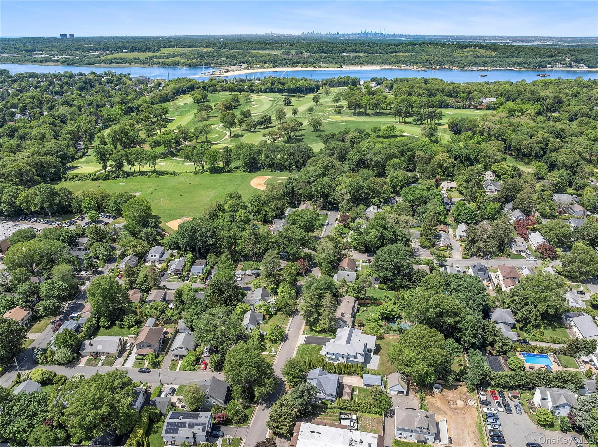Aerial perspective highlighting a residential area with mature trees, a golf course, a baseball field, and a significant body of water Aerial perspective highlighting a residential area with mature trees, a golf course, a baseball field, and a significant body of water
