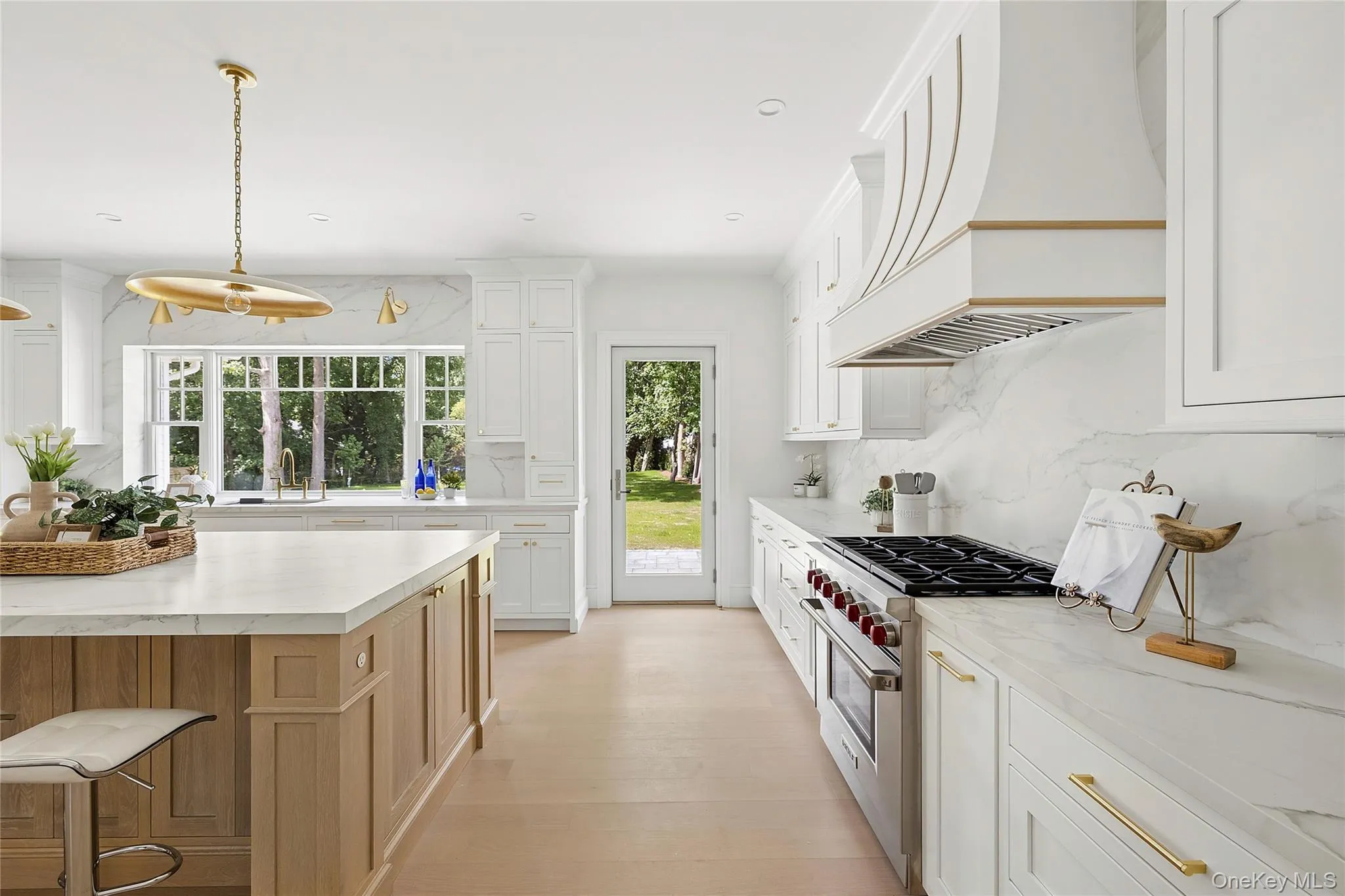 Spacious kitchen featuring an expansive island with a light wood finish, white shaker cabinetry, and light-toned countertops extending to a full-height backsplash Spacious kitchen featuring an expansive island with a light wood finish, white shaker cabinetry, and light-toned countertops extending to a full-height backsplash