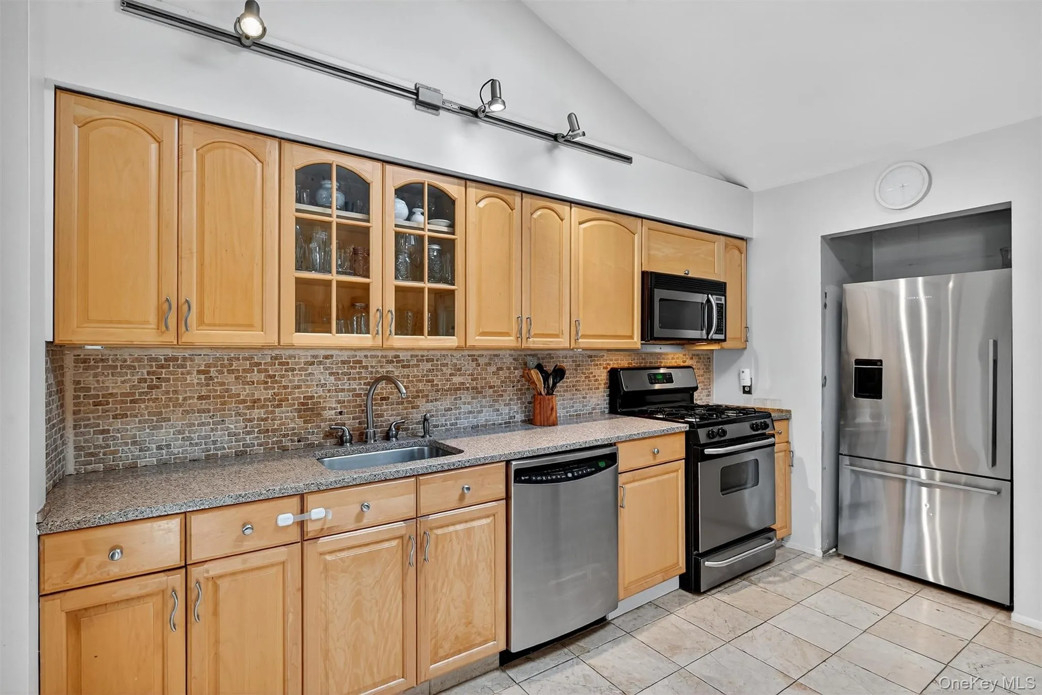 Kitchen featuring tasteful backsplash, appliances with stainless steel finishes, glass insert cabinets, light stone countertops, and light tile patterned floors Kitchen featuring tasteful backsplash, appliances with stainless steel finishes, glass insert cabinets, light stone countertops, and light tile patterned floors