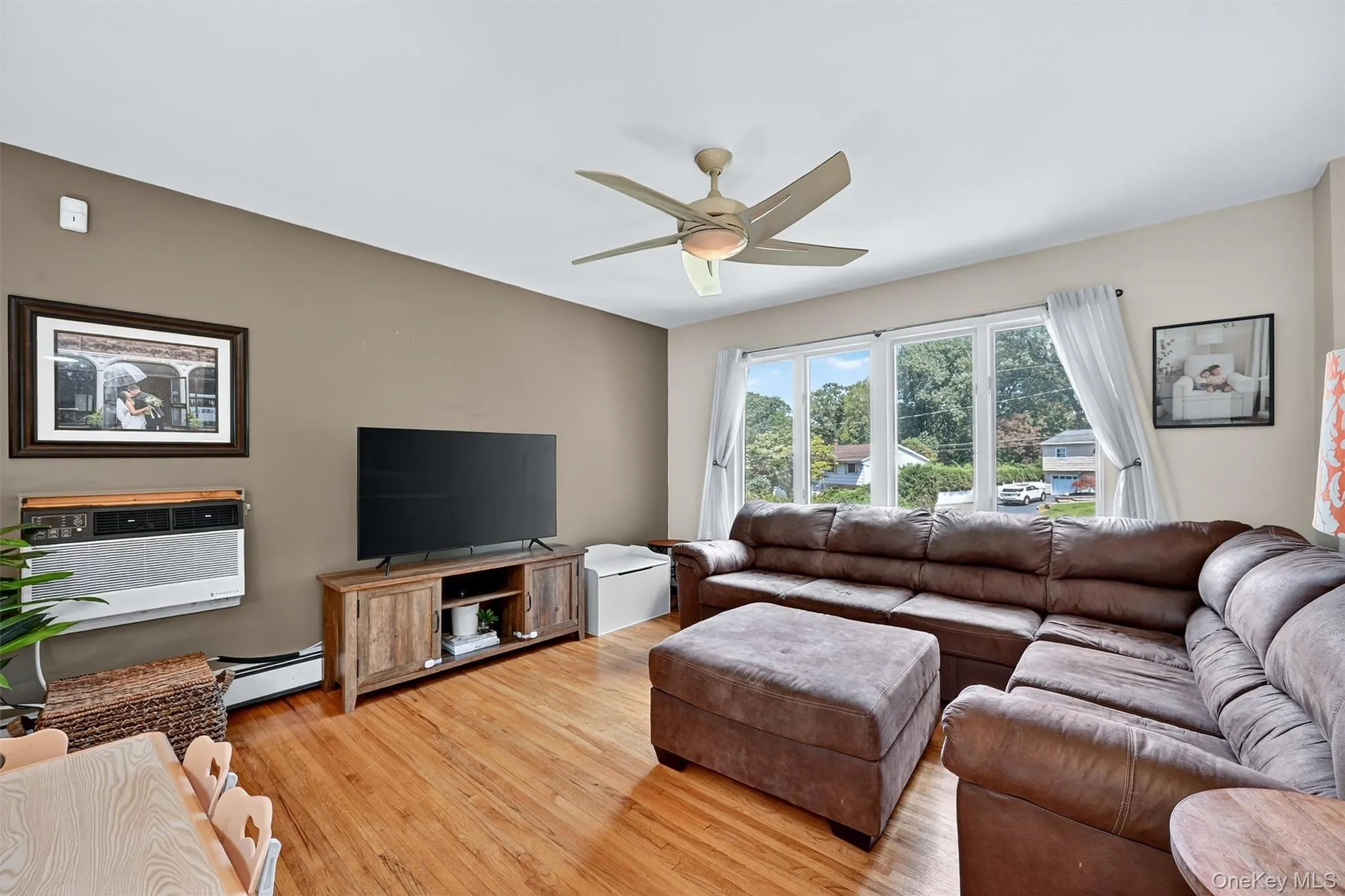 Living room with light wood-style flooring, ceiling fan, a baseboard radiator, and a wall unit AC Living room with light wood-style flooring, ceiling fan, a baseboard radiator, and a wall unit AC