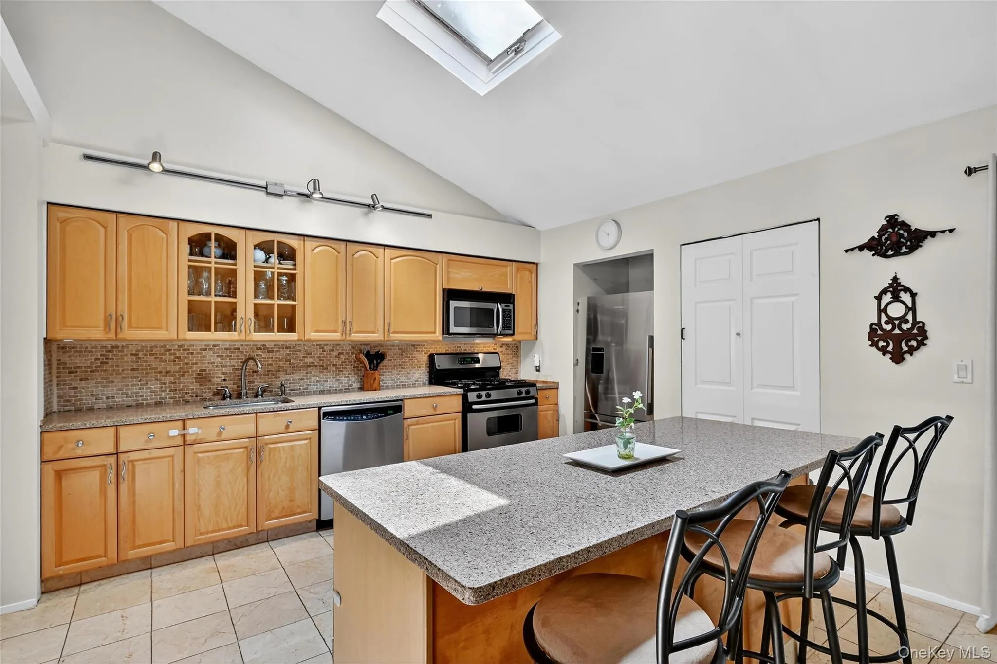 Kitchen featuring a skylight, lofted ceiling, stainless steel appliances, tasteful backsplash, and glass insert cabinets Kitchen featuring a skylight, lofted ceiling, stainless steel appliances, tasteful backsplash, and glass insert cabinets