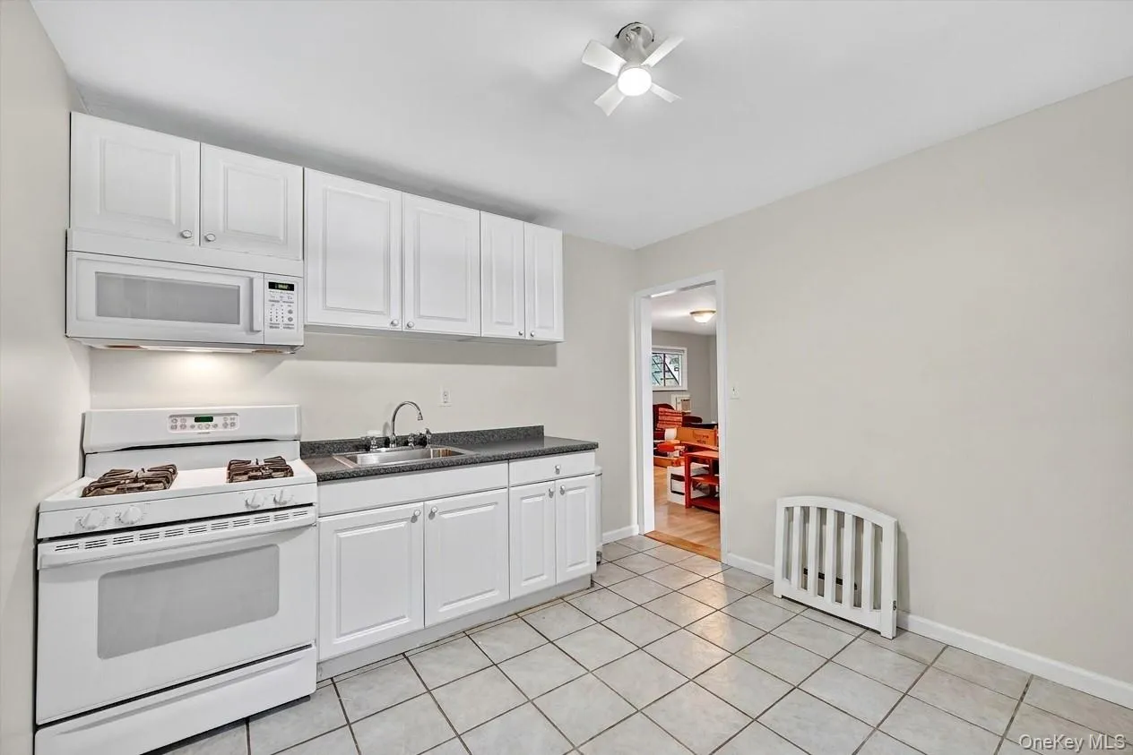 Kitchen featuring white appliances, dark countertops, white cabinetry, and light tile patterned flooring Kitchen featuring white appliances, dark countertops, white cabinetry, and light tile patterned flooring
