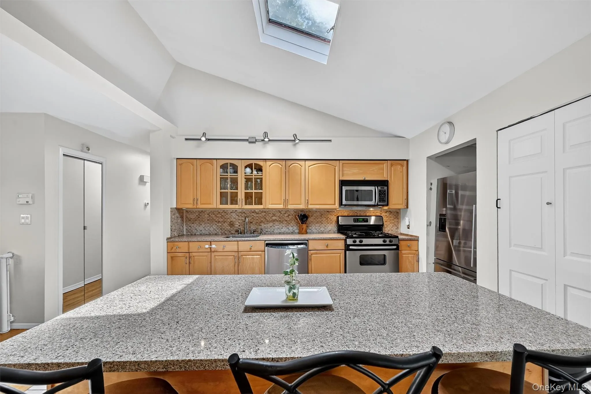 Kitchen with a breakfast bar, a skylight, stainless steel appliances, decorative backsplash, and vaulted ceiling Kitchen with a breakfast bar, a skylight, stainless steel appliances, decorative backsplash, and vaulted ceiling