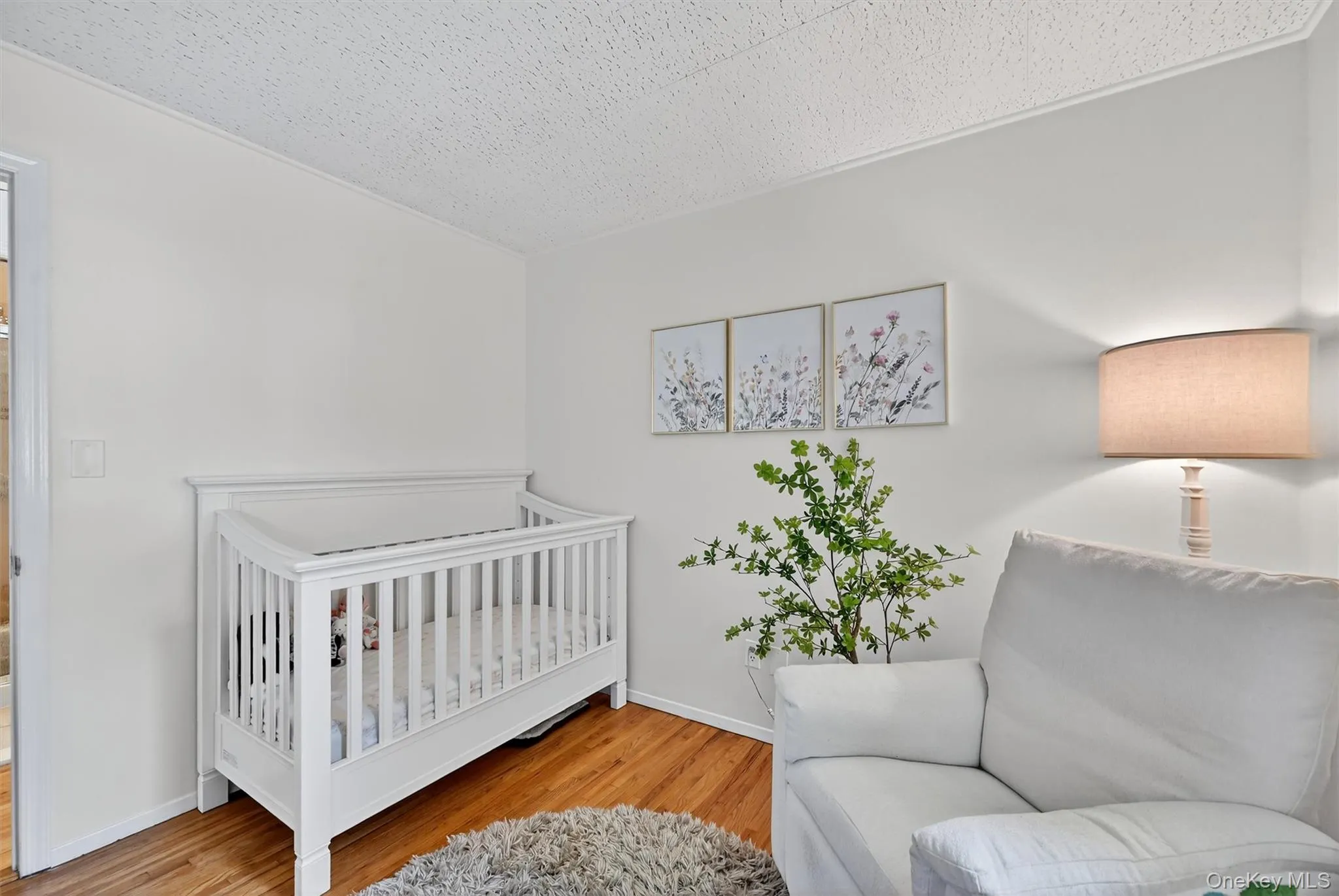 Bedroom with light wood-type flooring, a crib, and a textured ceiling Bedroom with light wood-type flooring, a crib, and a textured ceiling