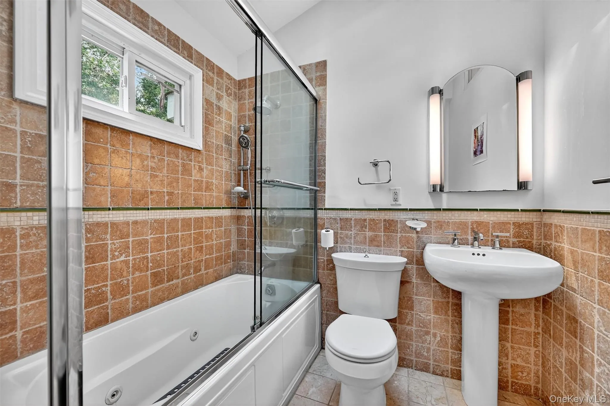 Full bathroom with combined bath / shower with glass door, tile walls, a wainscoted wall, and tile patterned flooring Full bathroom with combined bath / shower with glass door, tile walls, a wainscoted wall, and tile patterned flooring