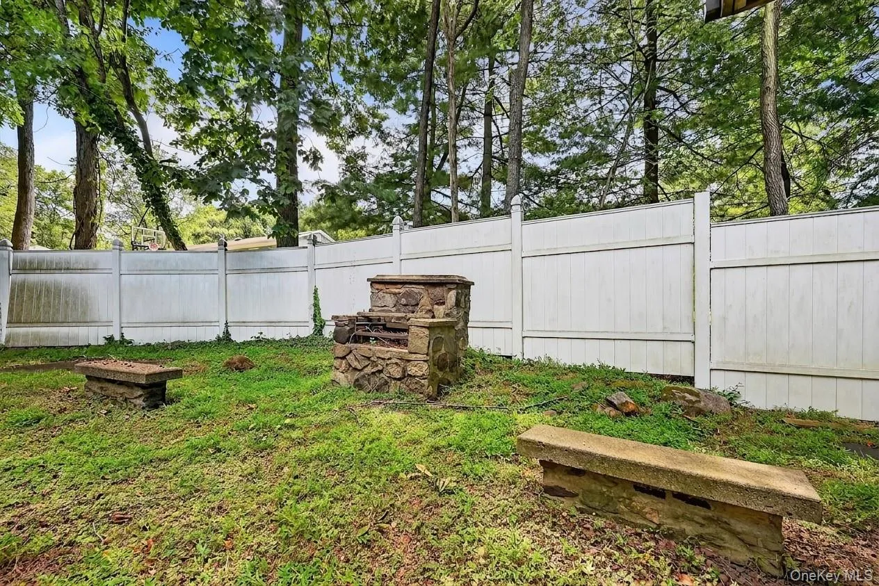 Backyard featuring a stone barbecue pit and two stone benches, enclosed by a white privacy fence Backyard featuring a stone barbecue pit and two stone benches, enclosed by a white privacy fence