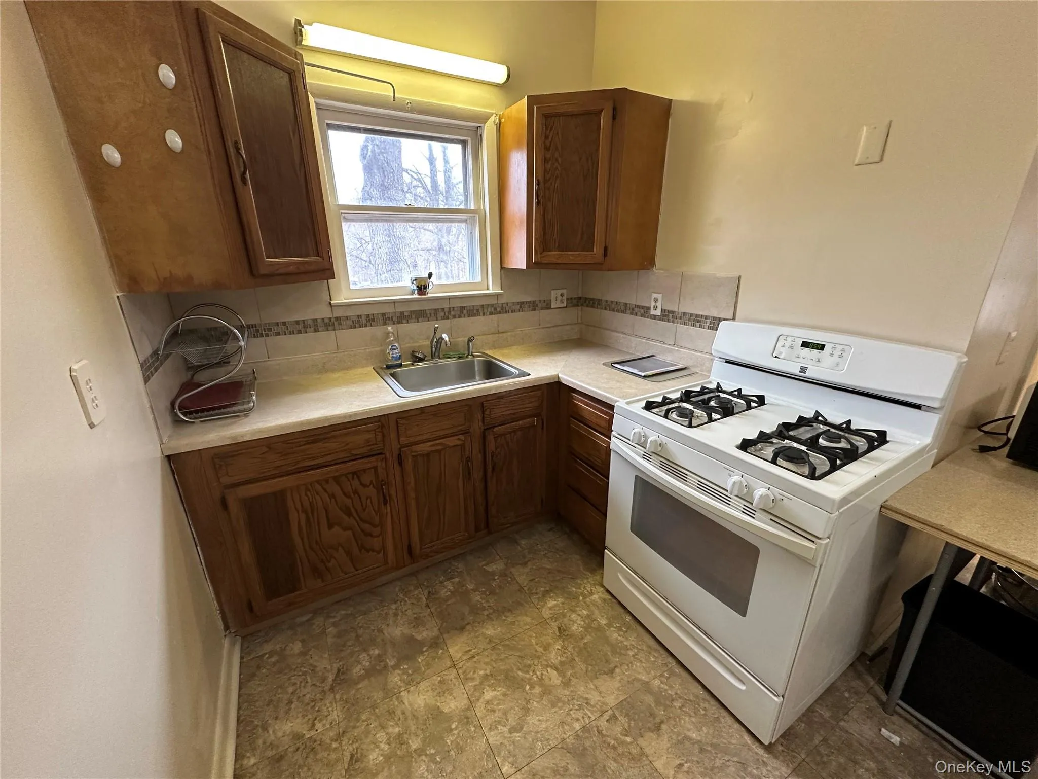 Kitchen with tasteful backsplash, light countertops, white range with gas stovetop, and a sink Kitchen with tasteful backsplash, light countertops, white range with gas stovetop, and a sink