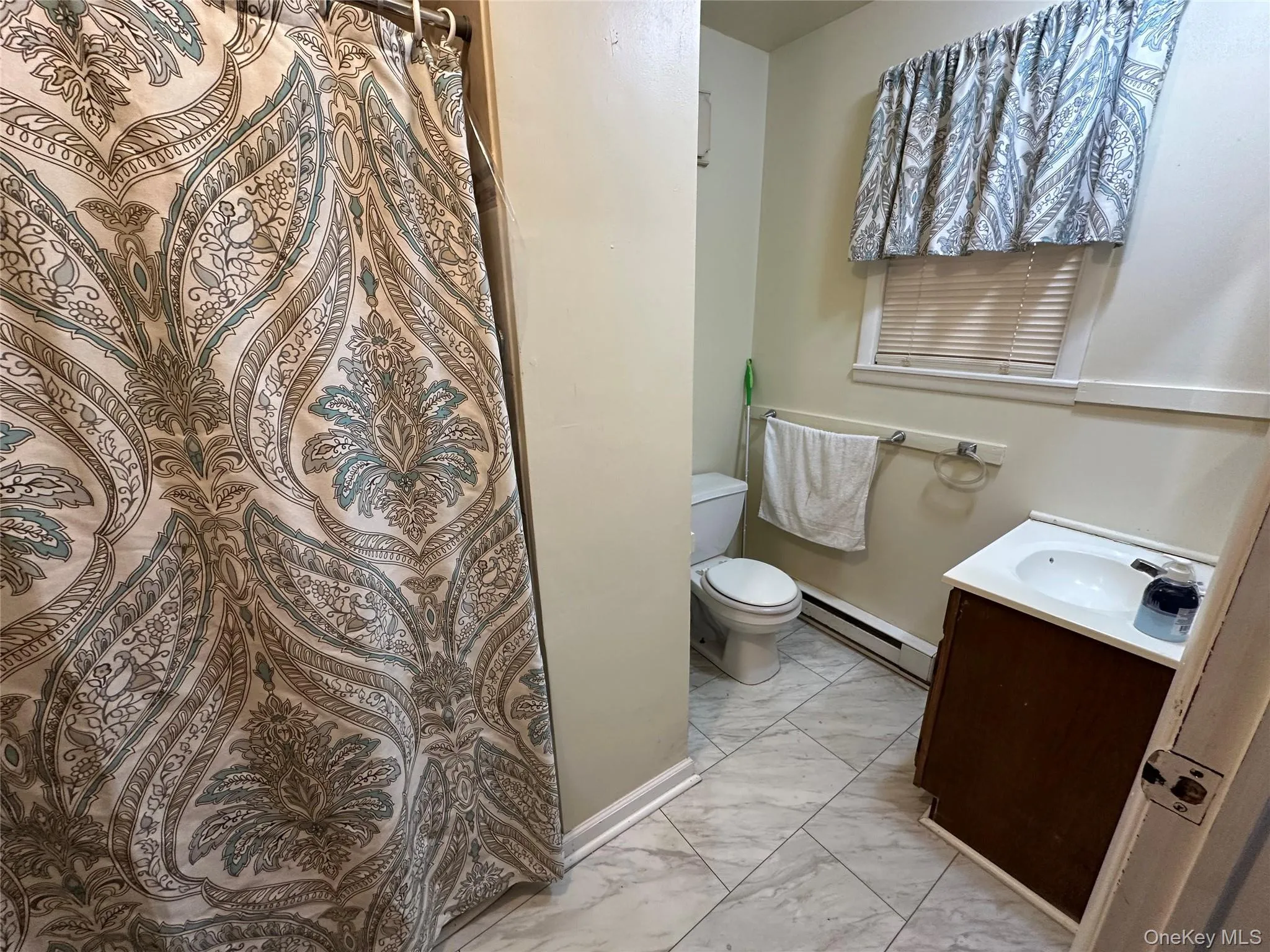 Bathroom featuring baseboards, toilet, baseboard heating, marble finish floor, and vanity Bathroom featuring baseboards, toilet, baseboard heating, marble finish floor, and vanity