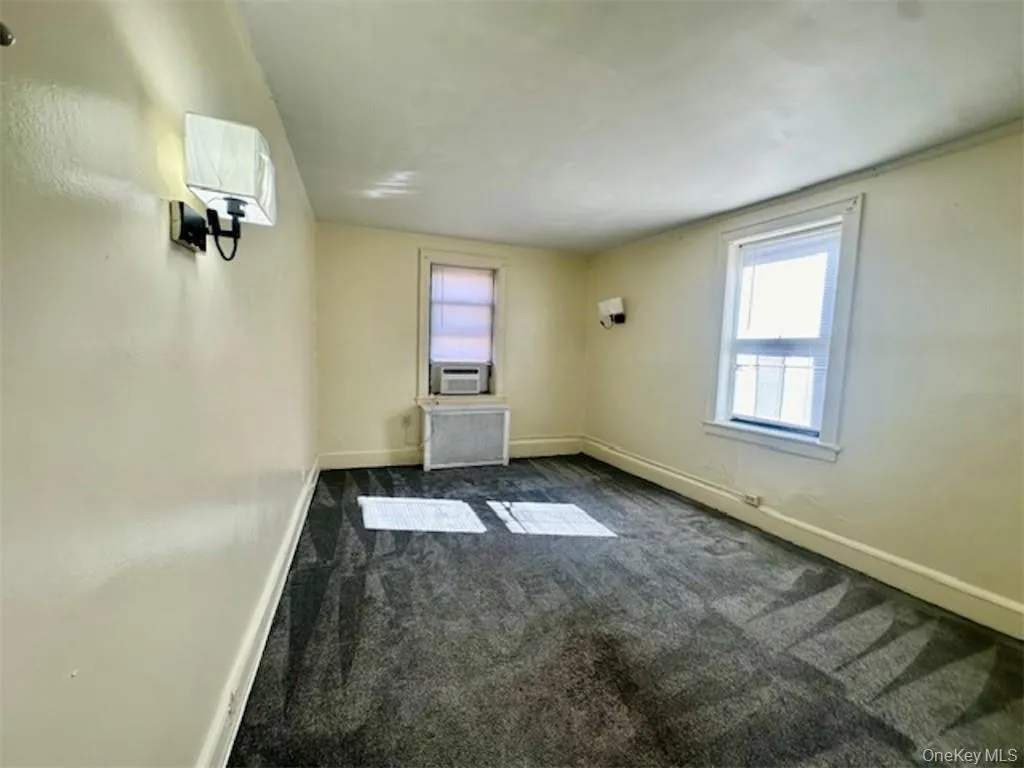 Empty room with plenty of natural light, cooling unit, and dark carpet Empty room with plenty of natural light, cooling unit, and dark carpet