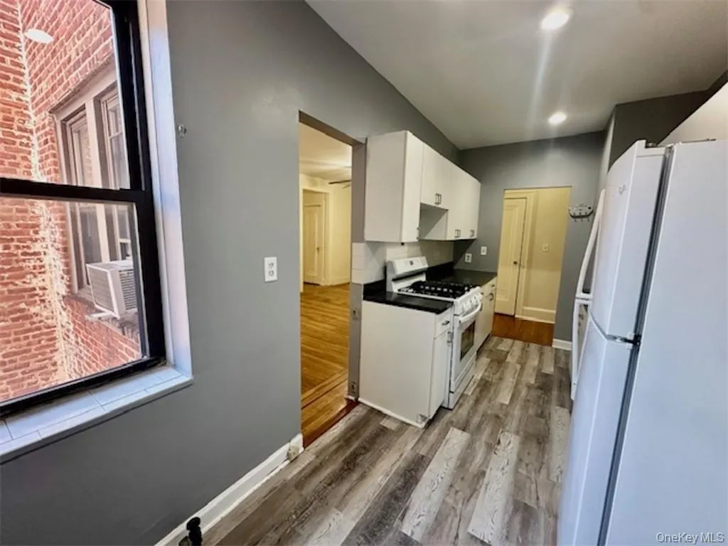 Kitchen with cooling unit, hardwood / wood-style flooring, white cabinetry, brick wall, and white appliances Kitchen with cooling unit, hardwood / wood-style flooring, white cabinetry, brick wall, and white appliances