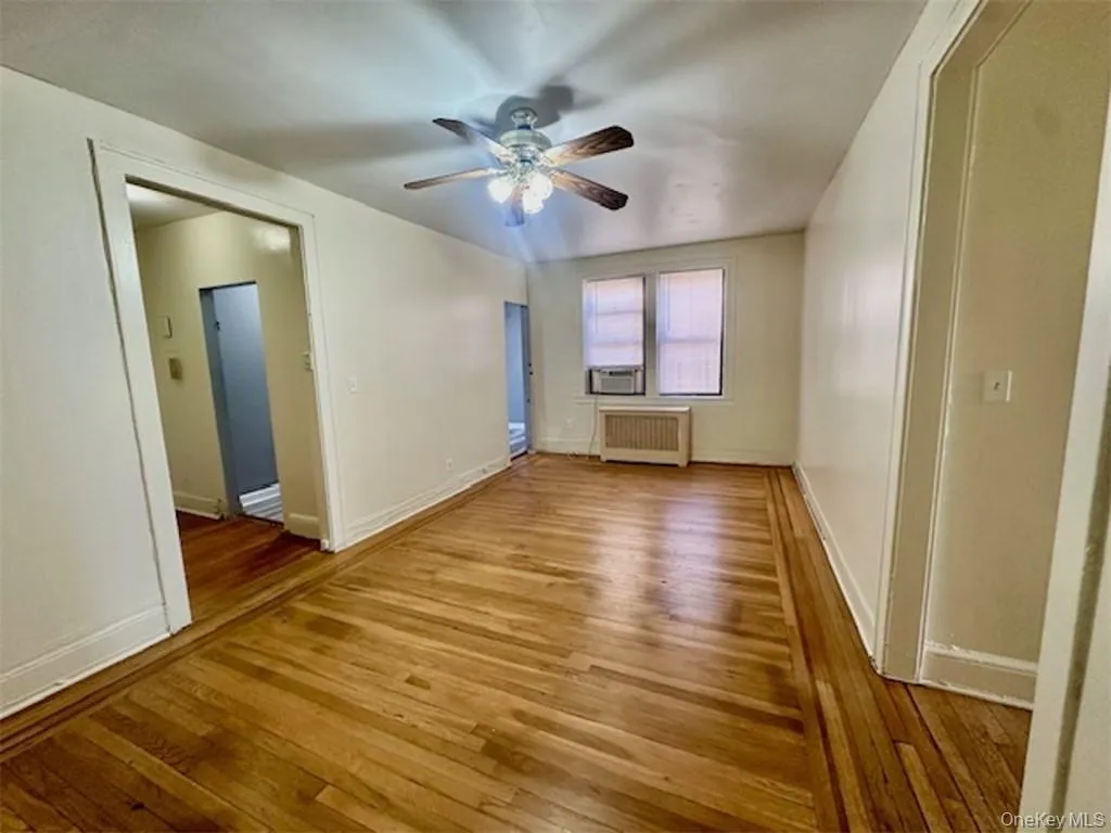 Unfurnished room featuring light hardwood / wood-style floors, ceiling fan, and radiator heating unit Unfurnished room featuring light hardwood / wood-style floors, ceiling fan, and radiator heating unit