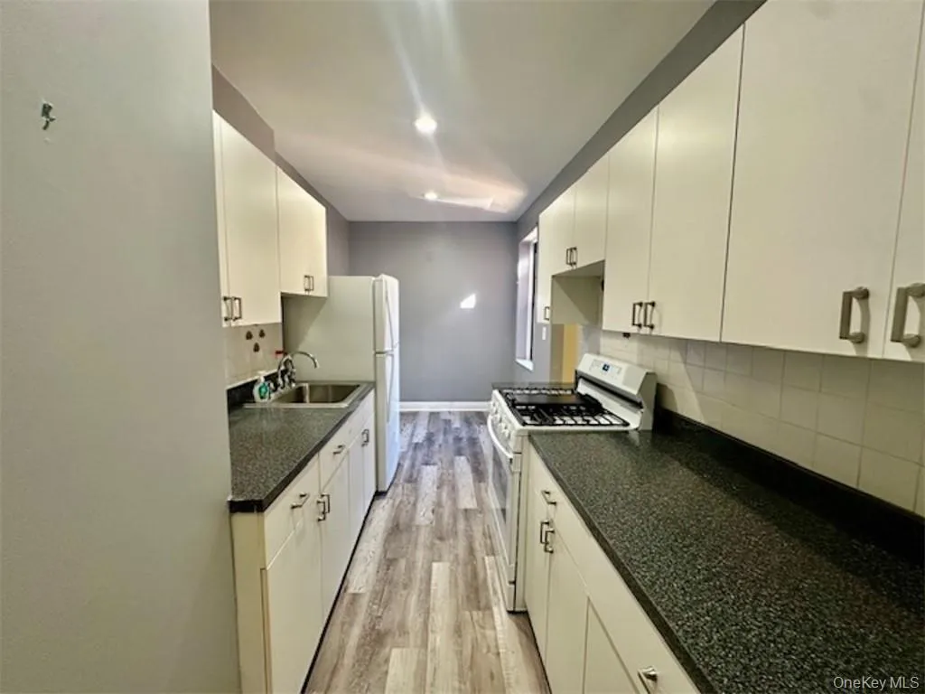 Kitchen featuring white gas range, white cabinetry, sink, and light hardwood / wood-style floors Kitchen featuring white gas range, white cabinetry, sink, and light hardwood / wood-style floors