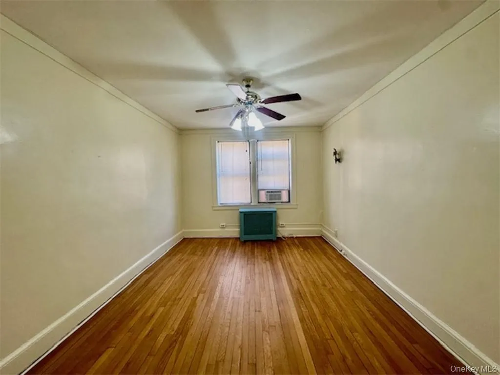 Unfurnished room featuring hardwood / wood-style flooring, radiator, ceiling fan, cooling unit, and crown molding Unfurnished room featuring hardwood / wood-style flooring, radiator, ceiling fan, cooling unit, and crown molding