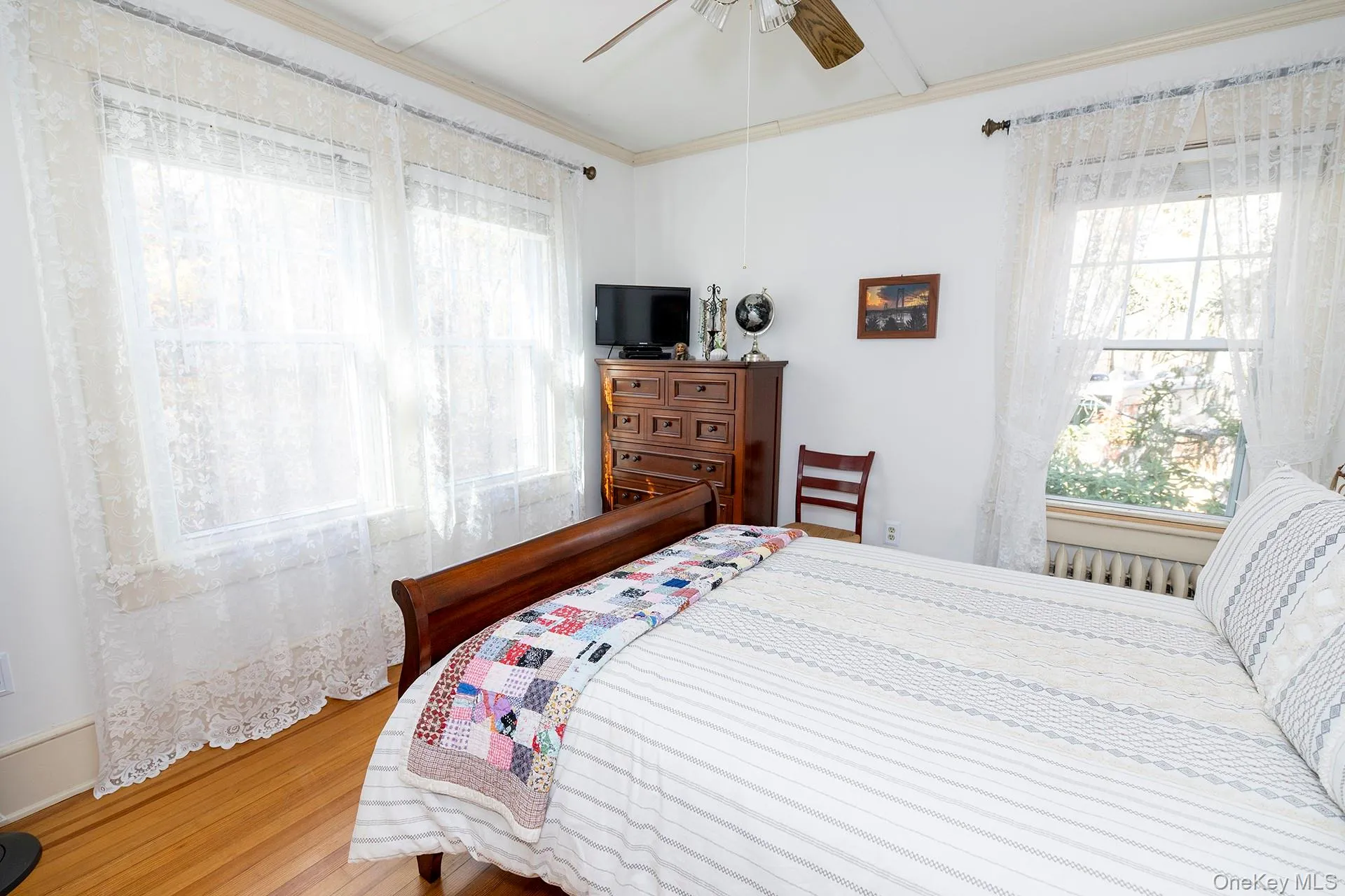 Bedroom with multiple windows, wood finished floors, ornamental molding, and a ceiling fan Bedroom with multiple windows, wood finished floors, ornamental molding, and a ceiling fan