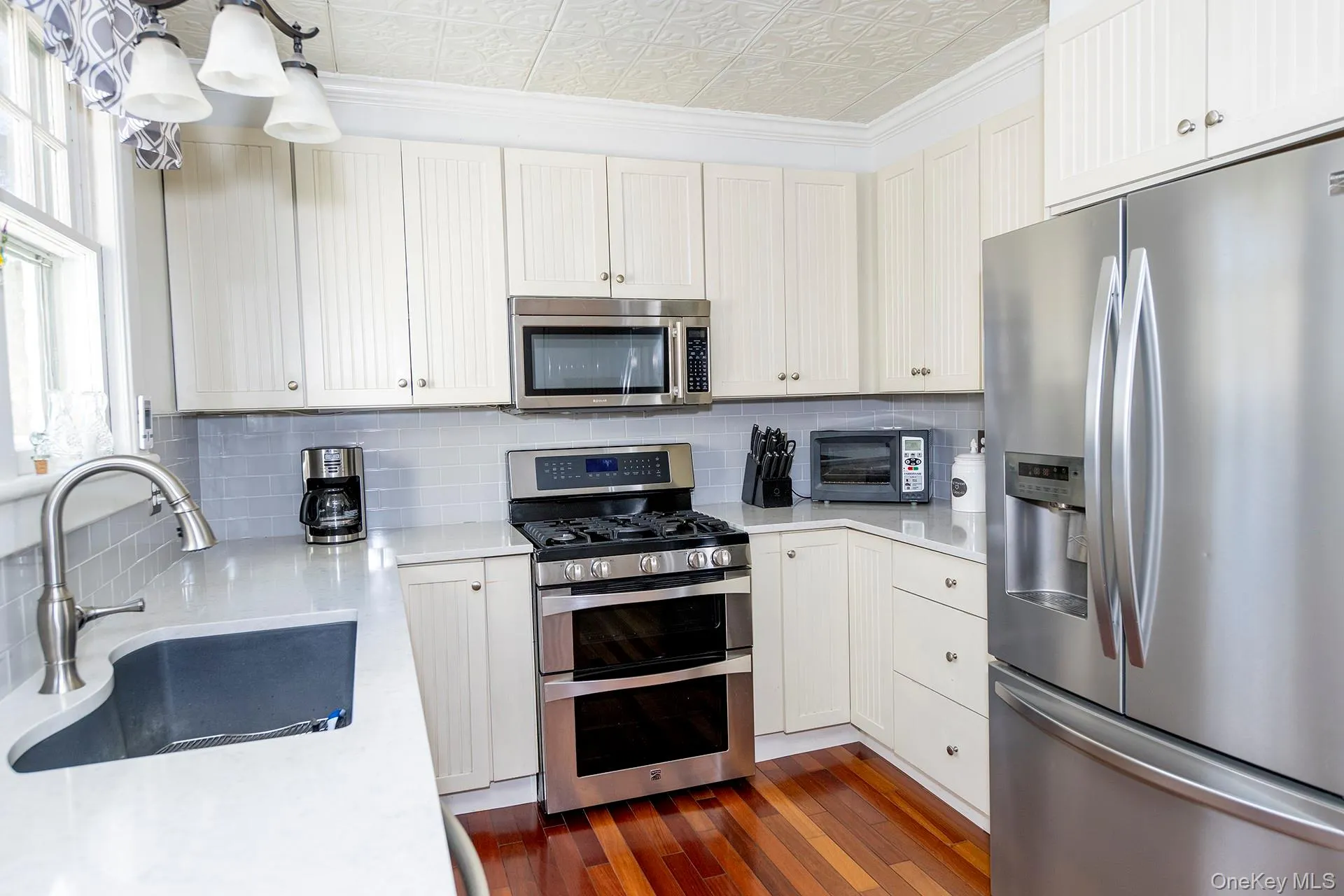 Kitchen featuring appliances with stainless steel finishes, an ornate ceiling, light stone counters, decorative backsplash, and dark wood-style flooring Kitchen featuring appliances with stainless steel finishes, an ornate ceiling, light stone counters, decorative backsplash, and dark wood-style flooring