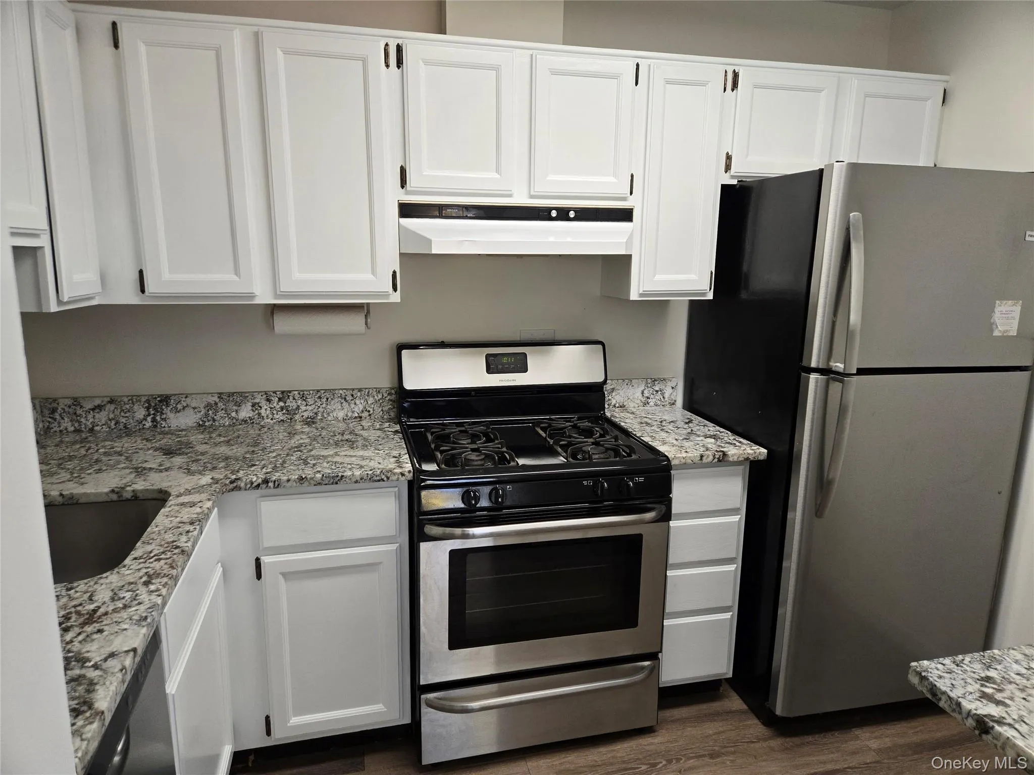 Kitchen with light stone countertops, white cabinets, dark hardwood / wood-style floors, and appliances with stainless steel finishes Kitchen with light stone countertops, white cabinets, dark hardwood / wood-style floors, and appliances with stainless steel finishes