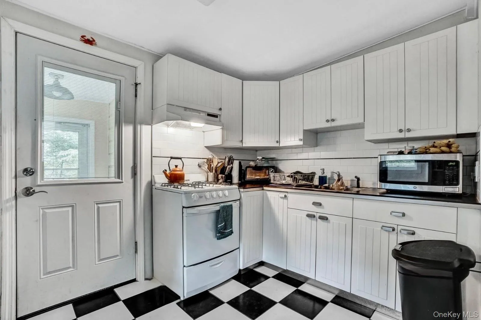 Kitchen featuring dark countertops, tile patterned floors, stainless steel microwave, under cabinet range hood, and gas range gas stove Kitchen featuring dark countertops, tile patterned floors, stainless steel microwave, under cabinet range hood, and gas range gas stove