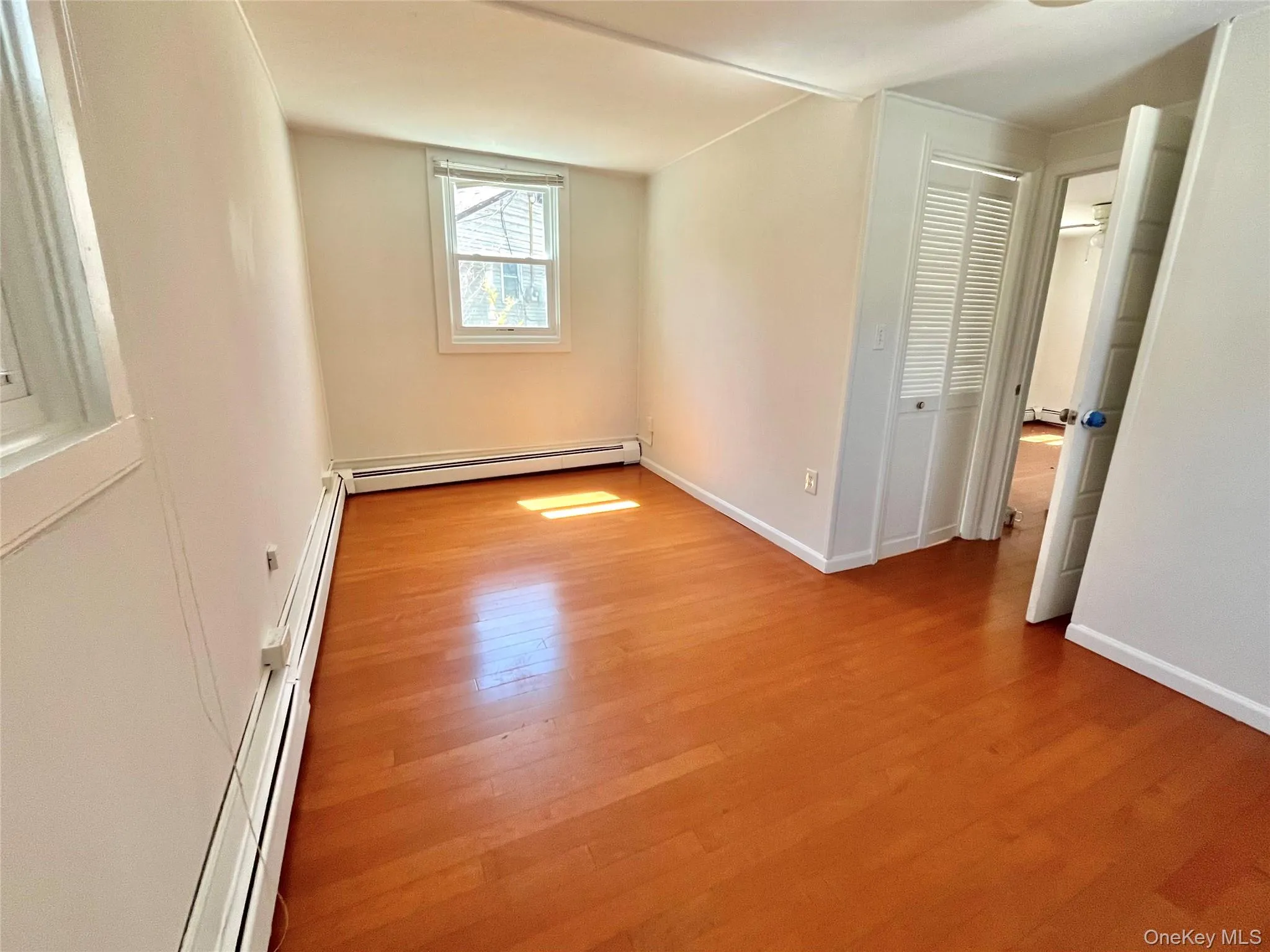 Unfurnished bedroom with baseboard heating, baseboards, and wood finished floors Unfurnished bedroom with baseboard heating, baseboards, and wood finished floors