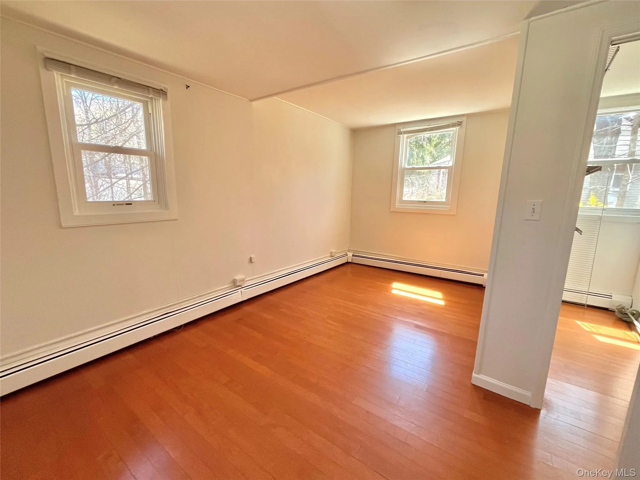 Empty room featuring a baseboard heating unit, hardwood / wood-style floors, baseboards, and baseboard heating Empty room featuring a baseboard heating unit, hardwood / wood-style floors, baseboards, and baseboard heating