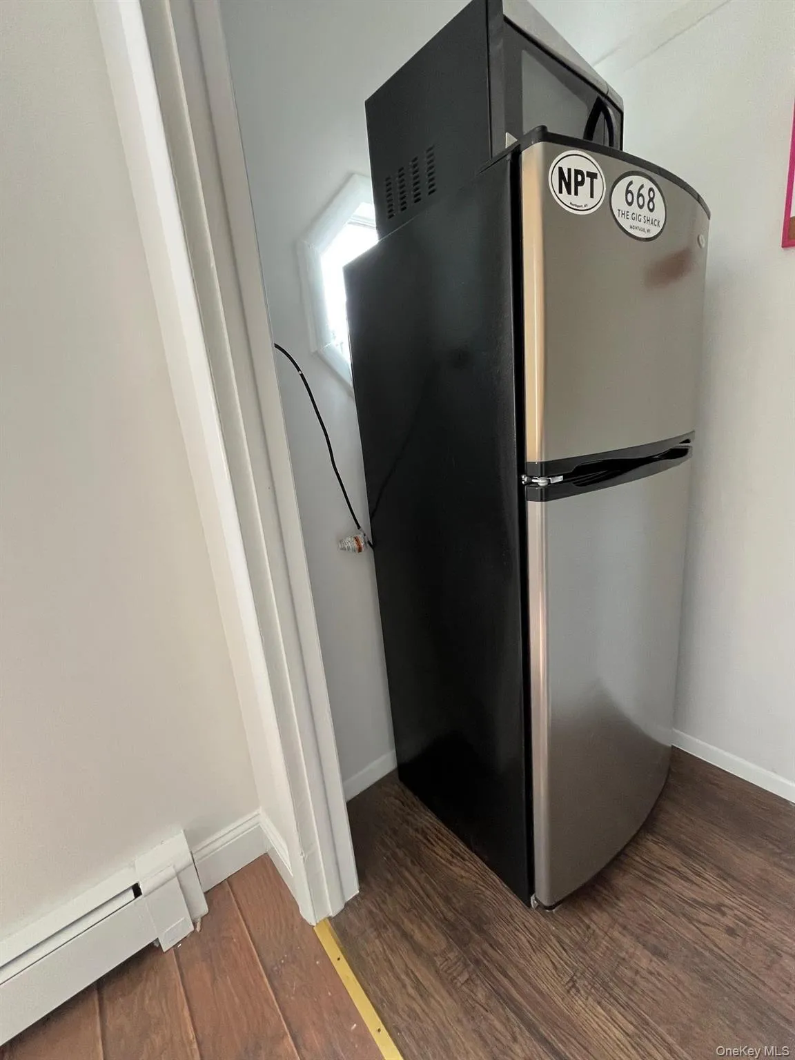 Details with freestanding refrigerator, dark wood-style flooring, baseboards, and a baseboard radiator Details with freestanding refrigerator, dark wood-style flooring, baseboards, and a baseboard radiator