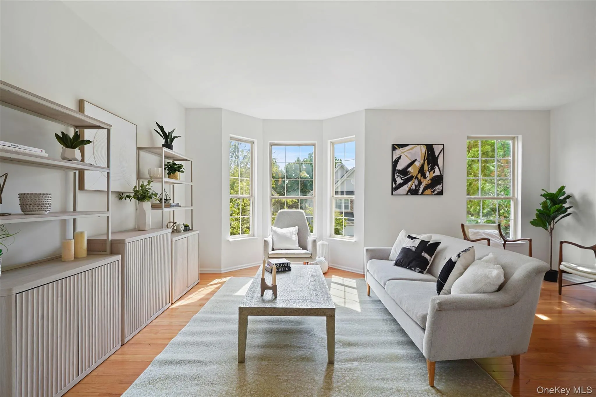 Bright living space featuring natural light, wood-finish flooring, a bay window, and built-in shelving with integrated cabinetry Bright living space featuring natural light, wood-finish flooring, a bay window, and built-in shelving with integrated cabinetry