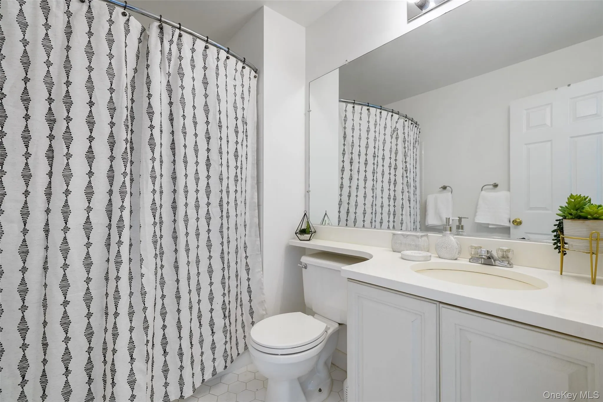 Bathroom featuring white hexagonal floor tiling, a toilet, and a vanity with a single sink and white cabinetry Bathroom featuring white hexagonal floor tiling, a toilet, and a vanity with a single sink and white cabinetry