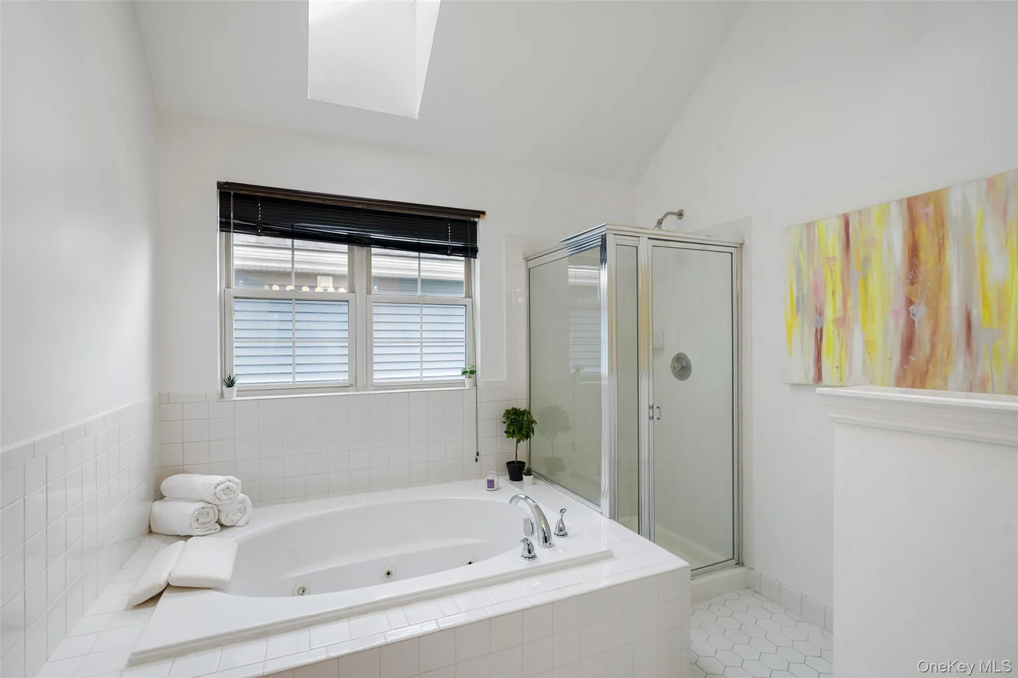 Primary spa-inspired bathroom featuring a built-in soaking tub, an enclosed glass shower, a skylight, and white hex tile flooring Primary spa-inspired bathroom featuring a built-in soaking tub, an enclosed glass shower, a skylight, and white hex tile flooring