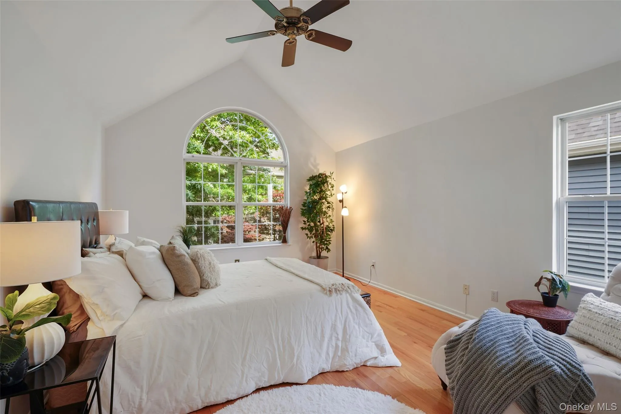 Primary with vaulted ceilings featuring a ceiling fan, arched window, and wood-finish flooring Primary with vaulted ceilings featuring a ceiling fan, arched window, and wood-finish flooring