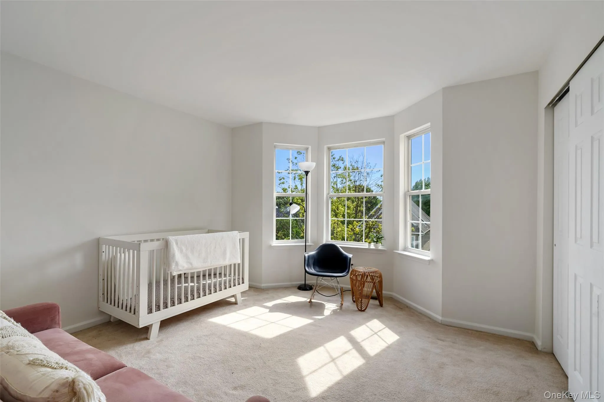 Room featuring a three-panel bay window, neutral-toned carpeting, and a bi-fold closet door Room featuring a three-panel bay window, neutral-toned carpeting, and a bi-fold closet door