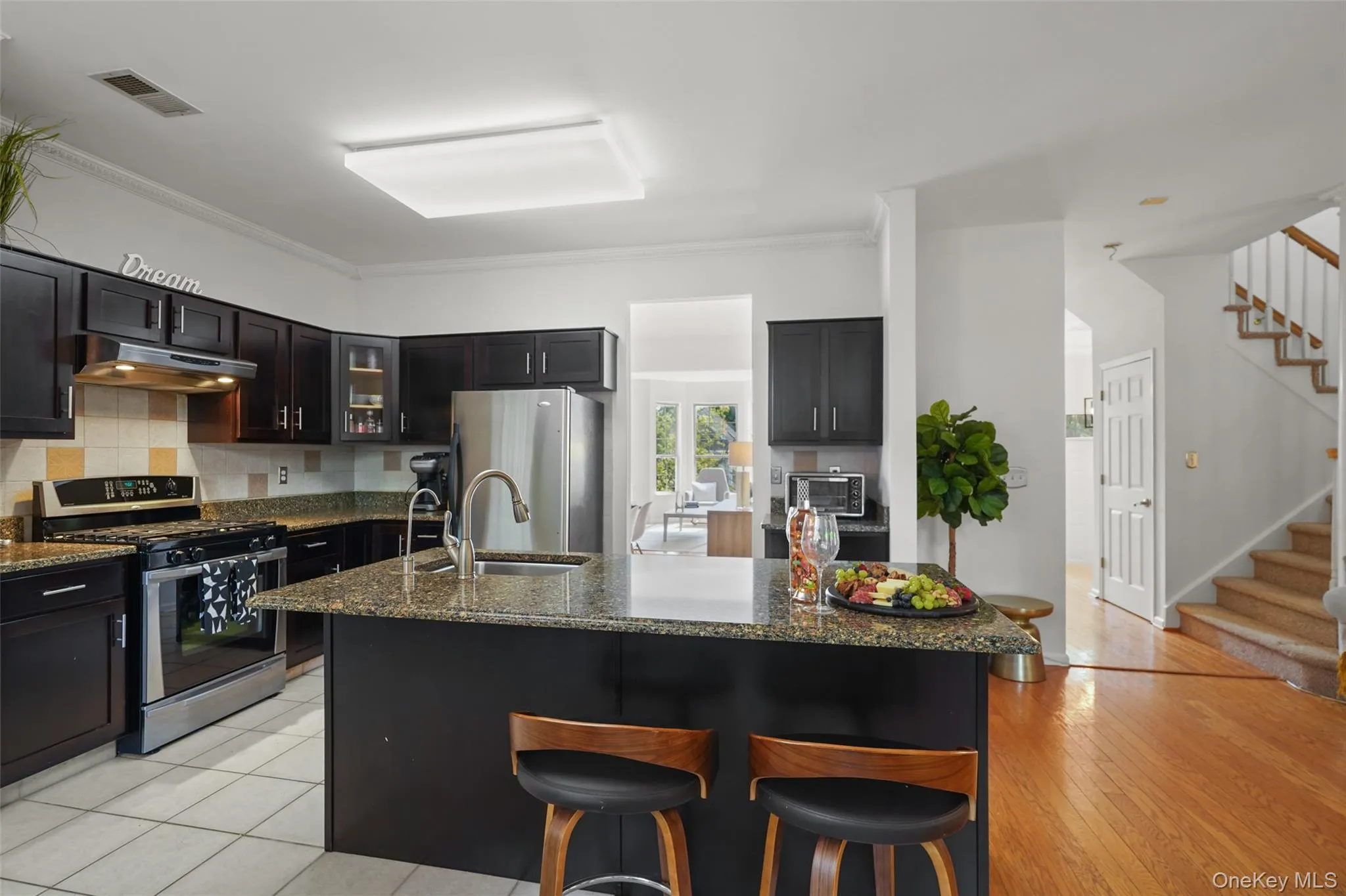 Kitchen featuring dark wood-finish cabinetry, stainless steel appliances, a center island with a granite-style countertop, and an undermount sink Kitchen featuring dark wood-finish cabinetry, stainless steel appliances, a center island with a granite-style countertop, and an undermount sink