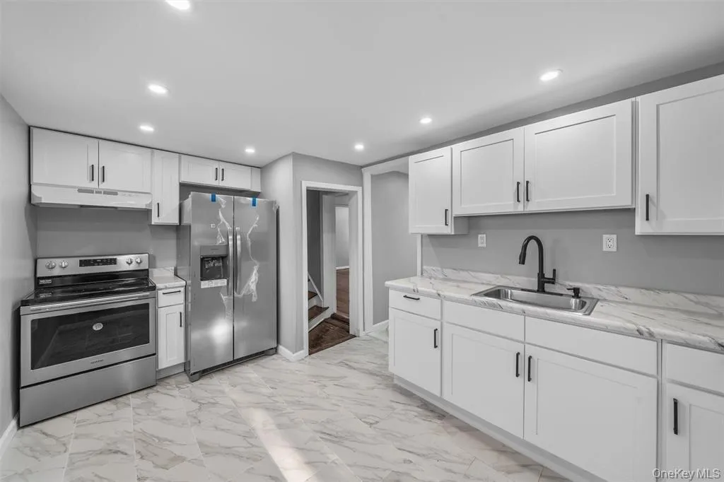 Contemporary kitchen featuring white cabinetry, stainless steel appliances, marble-look countertops, and recessed lighting Contemporary kitchen featuring white cabinetry, stainless steel appliances, marble-look countertops, and recessed lighting