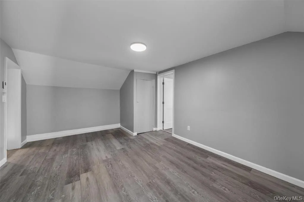Interior space featuring wood-finish flooring, light gray walls, white baseboards, a flush-mount ceiling light, and a white interior door Interior space featuring wood-finish flooring, light gray walls, white baseboards, a flush-mount ceiling light, and a white interior door