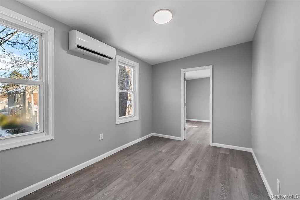 Room featuring wood-finish flooring, light gray walls, white trim, and a ceiling-mounted light fixture Room featuring wood-finish flooring, light gray walls, white trim, and a ceiling-mounted light fixture