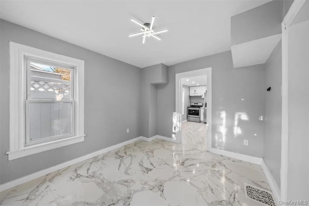 Room featuring marble-look flooring, light gray walls, a contemporary ceiling light fixture, and white trim Room featuring marble-look flooring, light gray walls, a contemporary ceiling light fixture, and white trim