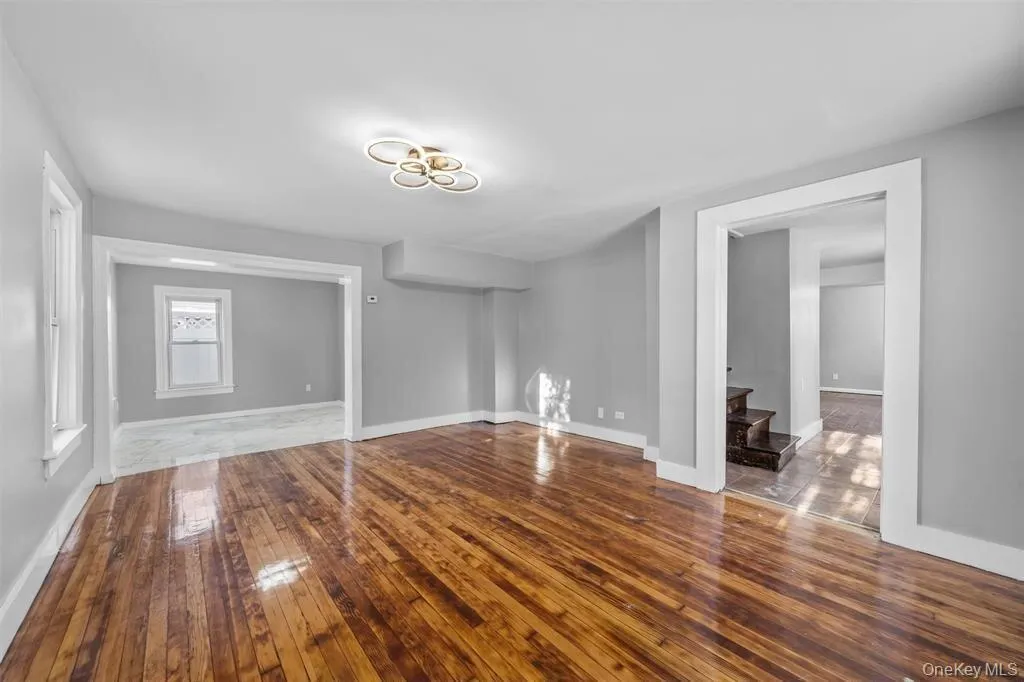 Spacious room with wood-finish flooring, light grey walls, and a contemporary ceiling fixture Spacious room with wood-finish flooring, light grey walls, and a contemporary ceiling fixture