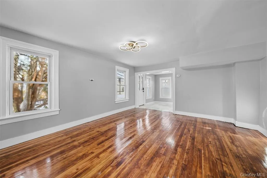 Spacious room featuring rich wood-finish flooring, light gray wall tones, and white trim Spacious room featuring rich wood-finish flooring, light gray wall tones, and white trim