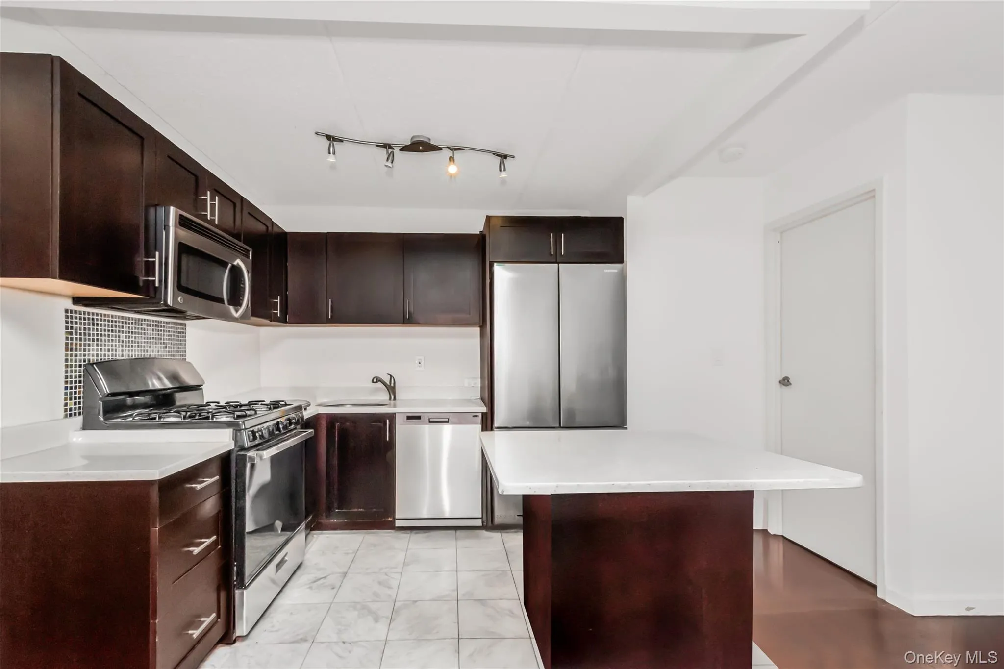 Kitchen featuring dark wood cabinetry, white countertops, stainless steel appliances, and a central island with a white counter Kitchen featuring dark wood cabinetry, white countertops, stainless steel appliances, and a central island with a white counter