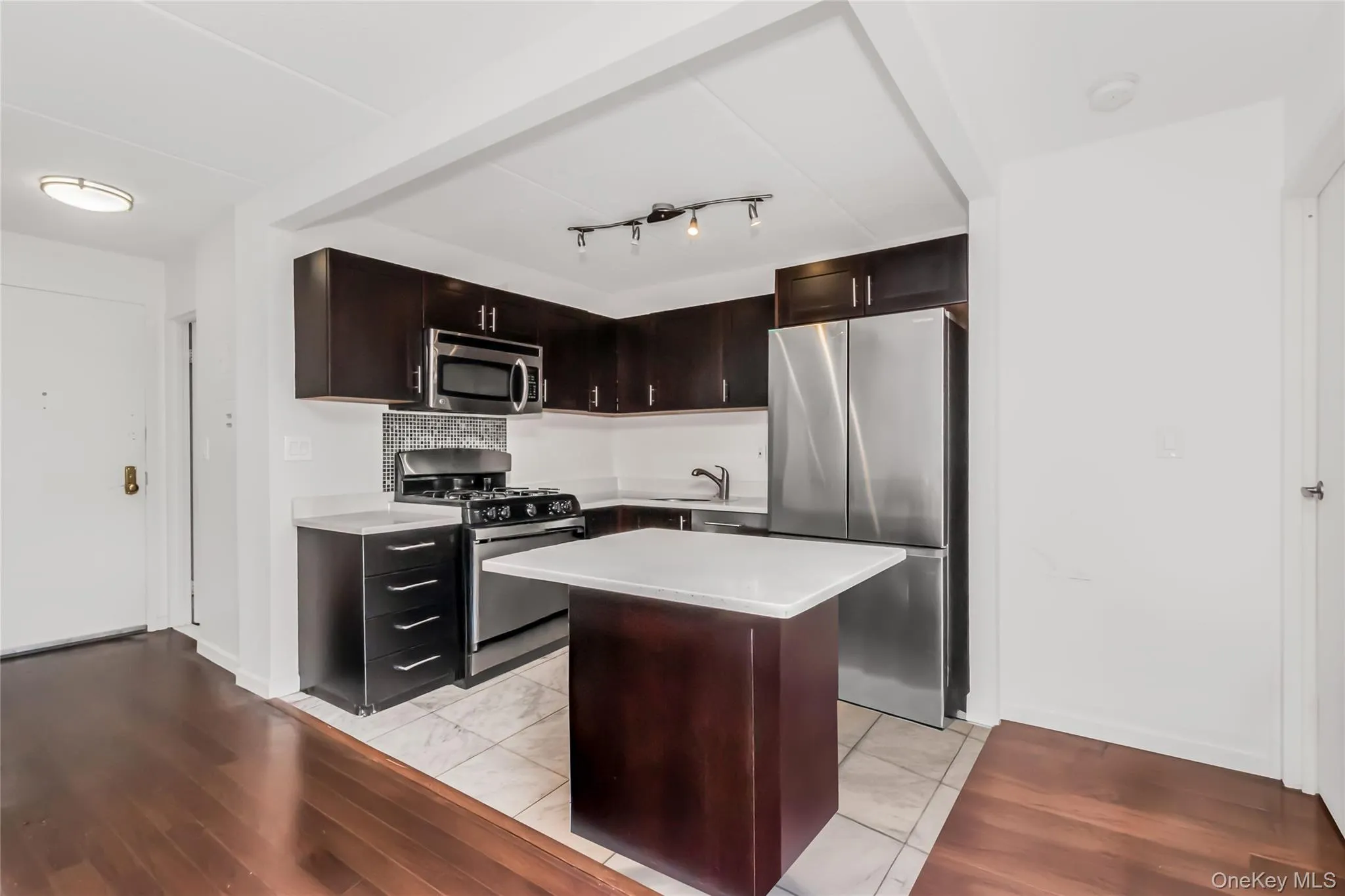 Kitchen featuring dark wood cabinetry, white countertops, stainless steel appliances, and a central island with a white counter Kitchen featuring dark wood cabinetry, white countertops, stainless steel appliances, and a central island with a white counter