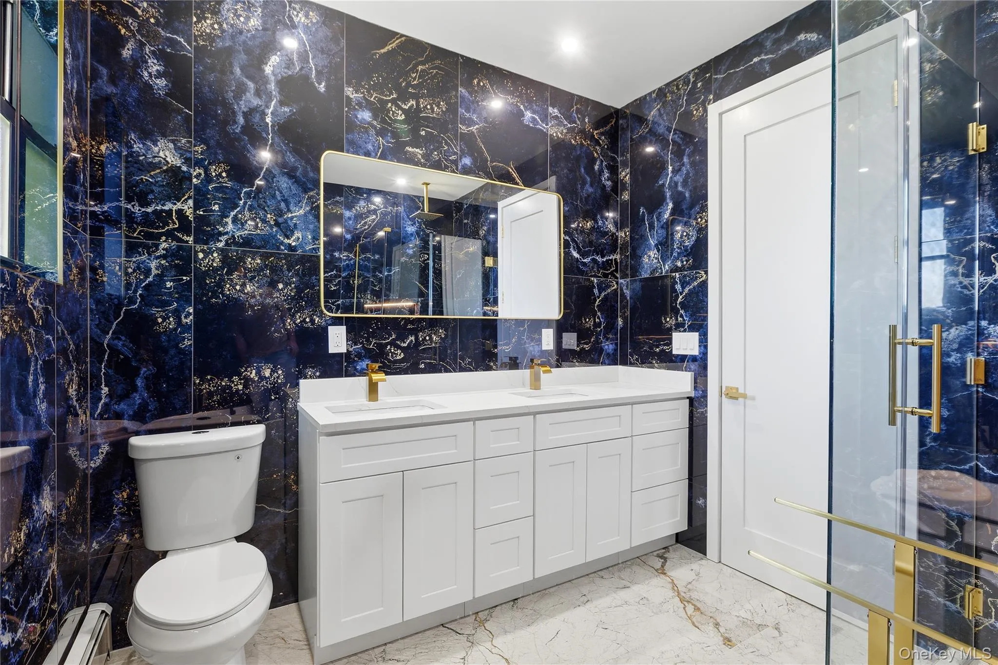 Bathroom with dark blue and gold veined wall tiles, white double vanity with gold-tone faucets, and a glass-enclosed shower with gold-tone hardware Bathroom with dark blue and gold veined wall tiles, white double vanity with gold-tone faucets, and a glass-enclosed shower with gold-tone hardware