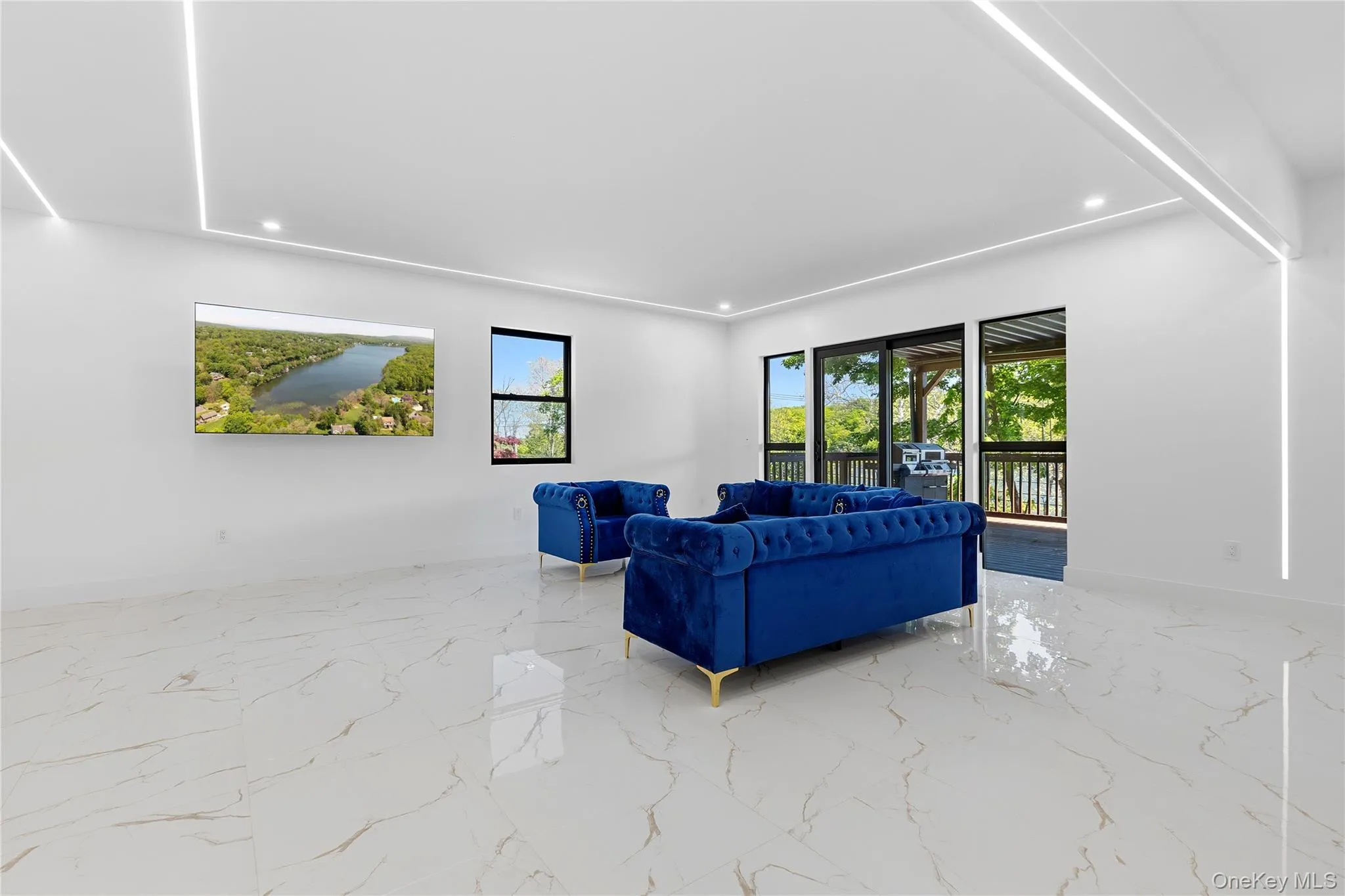 Spacious living area featuring polished tile flooring, recessed linear lighting, a large window, and sliding glass doors opening to an exterior deck Spacious living area featuring polished tile flooring, recessed linear lighting, a large window, and sliding glass doors opening to an exterior deck